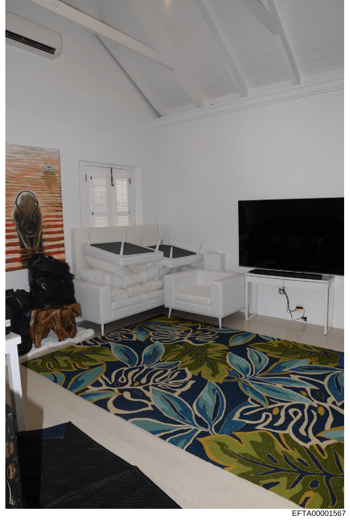 This photograph shows an interior living space featuring modern white sectional seating, a flat-screen television, decorative artwork, and a patterned area rug in blue, green, and cream tones. The room appears to be part of a residential property, wi