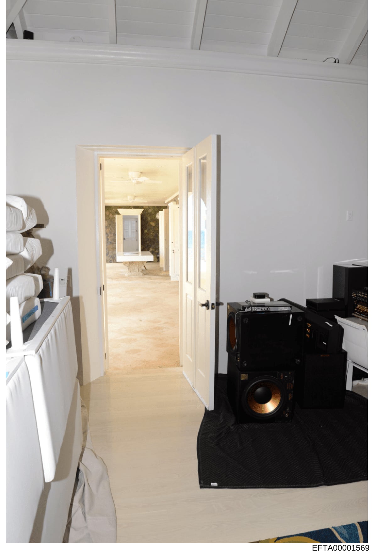 This is a photograph showing an interior hallway of a residential property, with views into what appears to be a bathroom area. The image captures white-painted walls, cream-colored doors, light wood flooring, and various items including towel storag