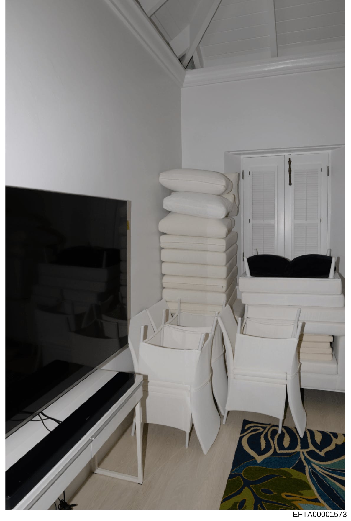 This is a photograph of an interior room space showing organized storage of white linens, towels, and bedding materials stacked on shelving and in white storage containers. A flat-screen television is visible on the left side of the frame. The image