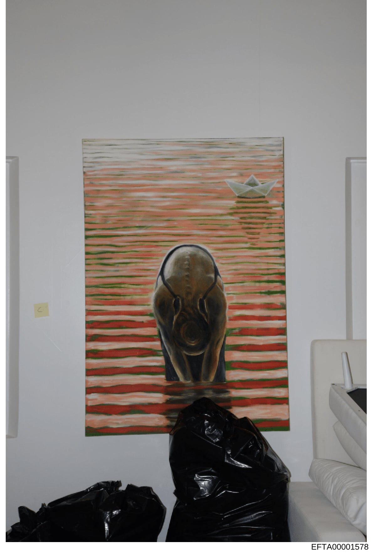 This is an evidence photograph showing the interior of a room with artwork hung on a white wall. The painting features a stylized bear figure in the foreground against a horizontally-striped background in red, green, and tan tones, with a paper boat 
