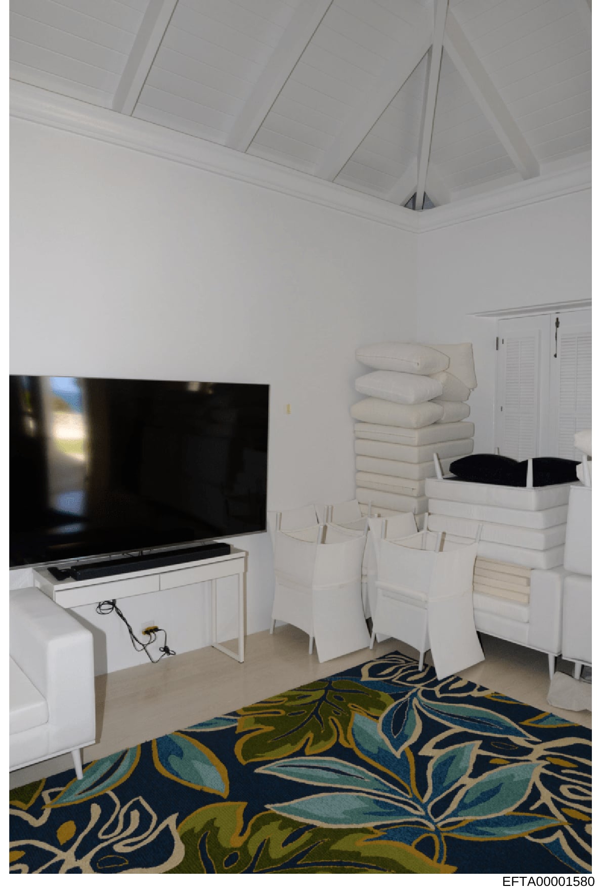 This is a photograph of a modern bedroom interior featuring white furniture, stacked linens, a large flat-screen television, and contemporary décor. The image appears to be documentation of a property's interior, likely taken during an investigation
