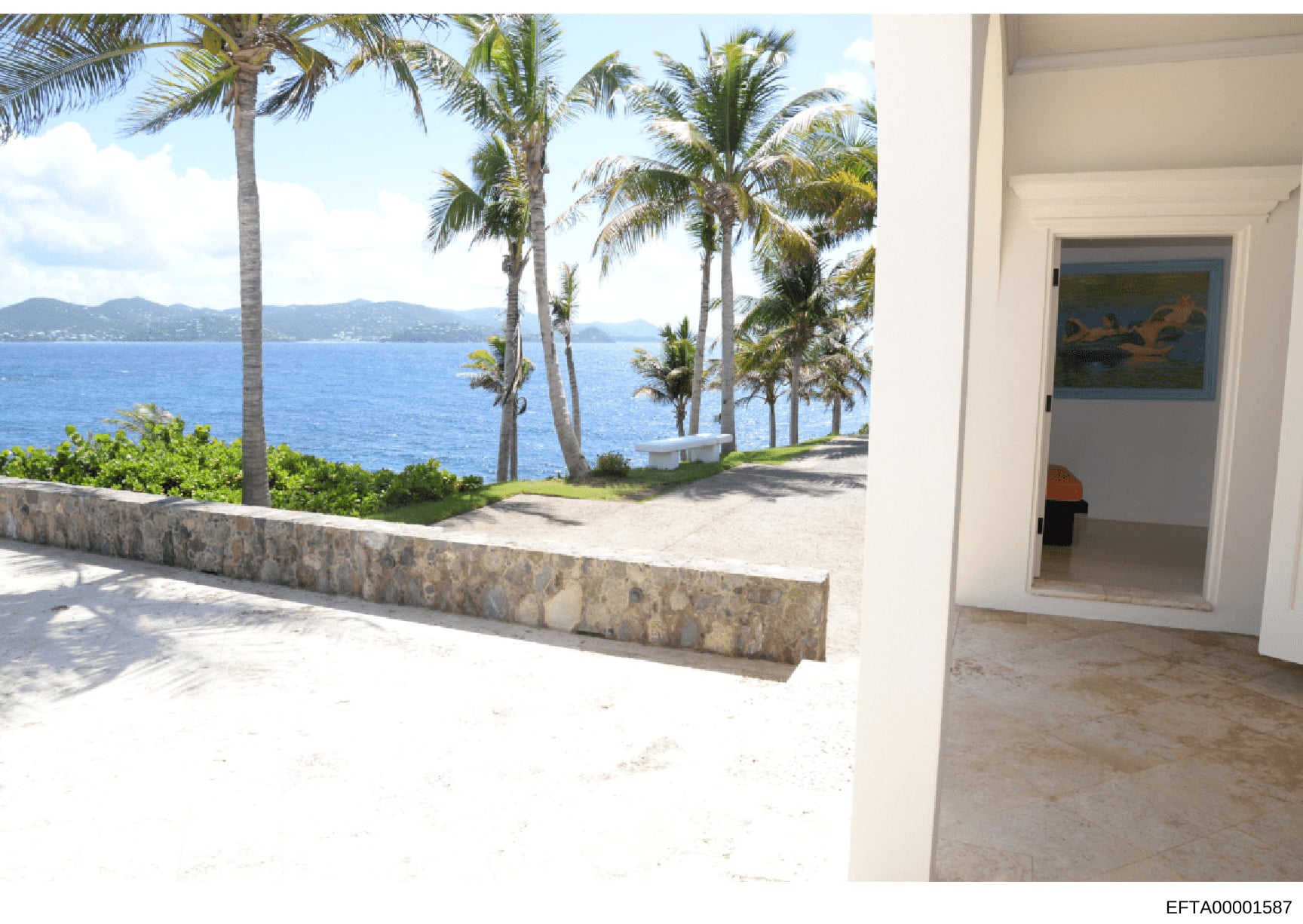 This photograph shows a beachfront or oceanfront property featuring a modern patio or deck area with direct views of the ocean, palm trees, and distant mountains. The image captures both interior and exterior spaces, including what appears to be a do