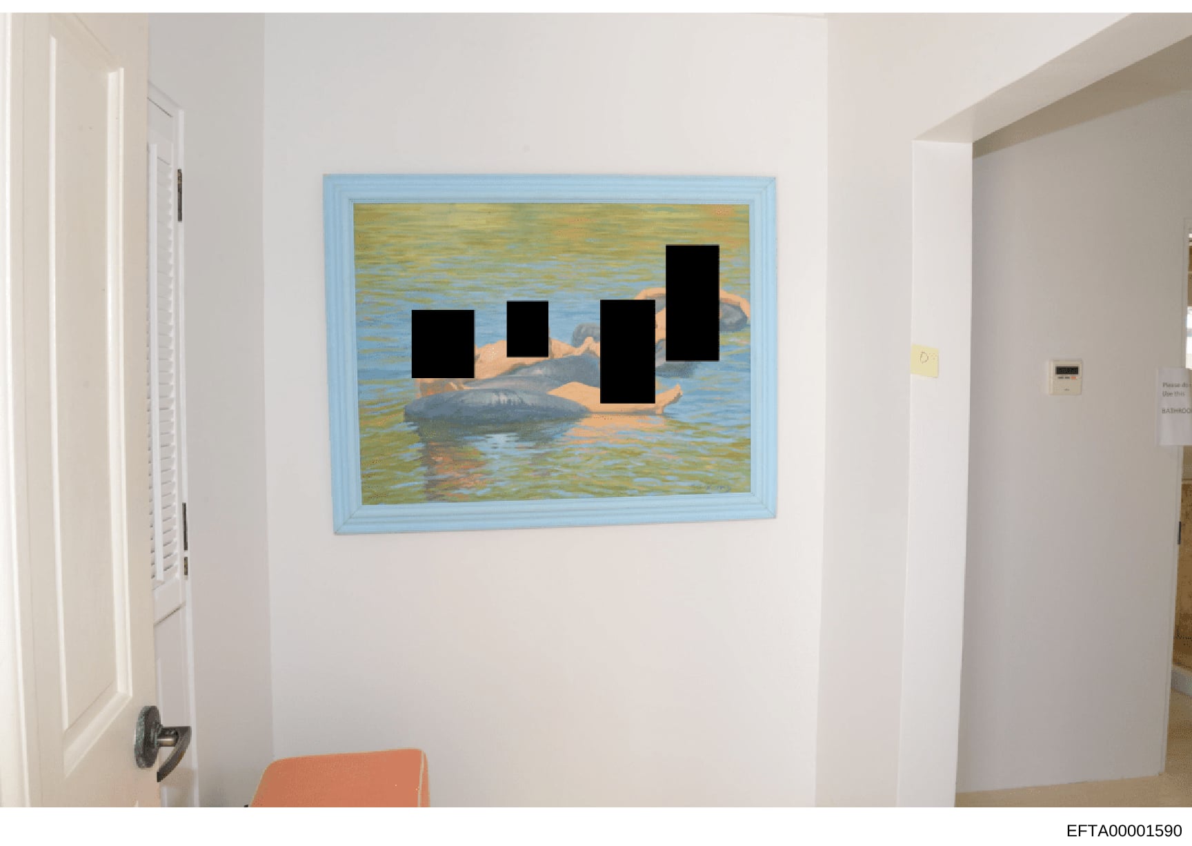 This is a photograph of an interior room showing a framed painting with a blue border hung on a white wall. The painting depicts a water scene with figures, with portions redacted by black rectangles. The photo appears to be evidence documentation of