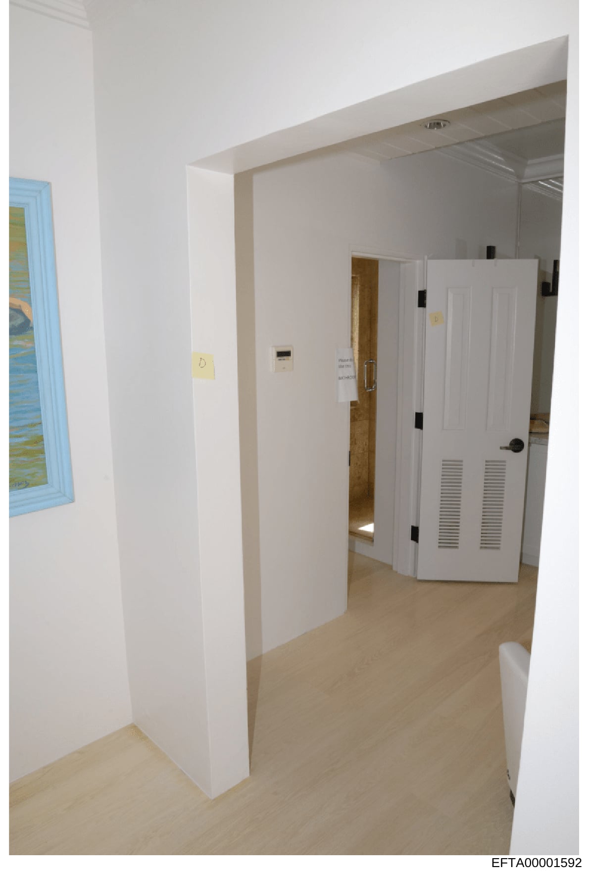 This is an evidence photograph showing the interior of a residential space, depicting a hallway with white walls, light wood flooring, and multiple white closet/cabinet doors with ventilation slits. Yellow evidence markers are visible on the walls. T