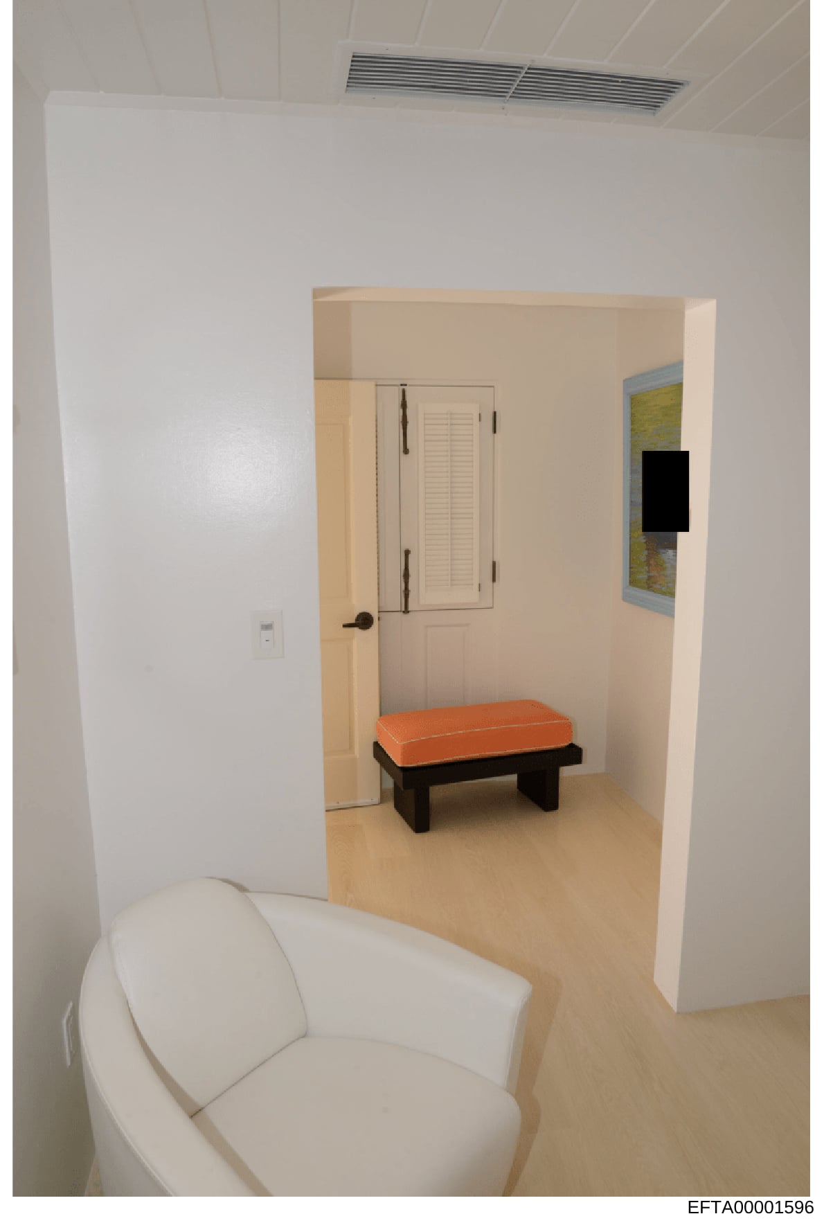 This is a photograph of an interior room showing modern, minimalist design. The space features white walls, beige flooring, a white curved chair in the foreground, a black bench with orange cushion, and a closet with louvered doors. A map or artwork 