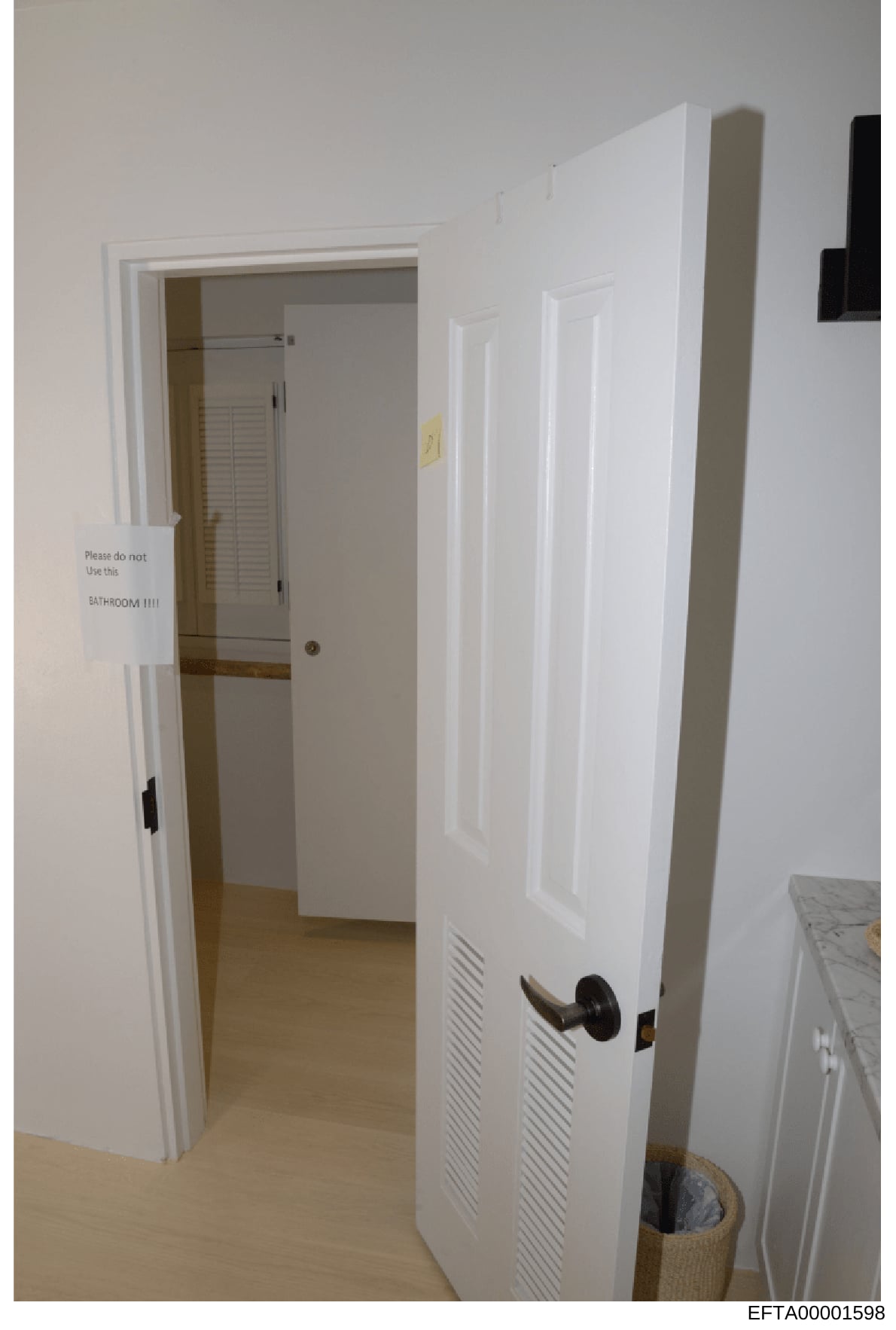 This is a photograph of an interior hallway with white walls and doors, including a bathroom entrance marked with a handwritten sign reading 'Please do not Use this BATHROOM!!!!' This appears to be evidence documentation from a property search or ins