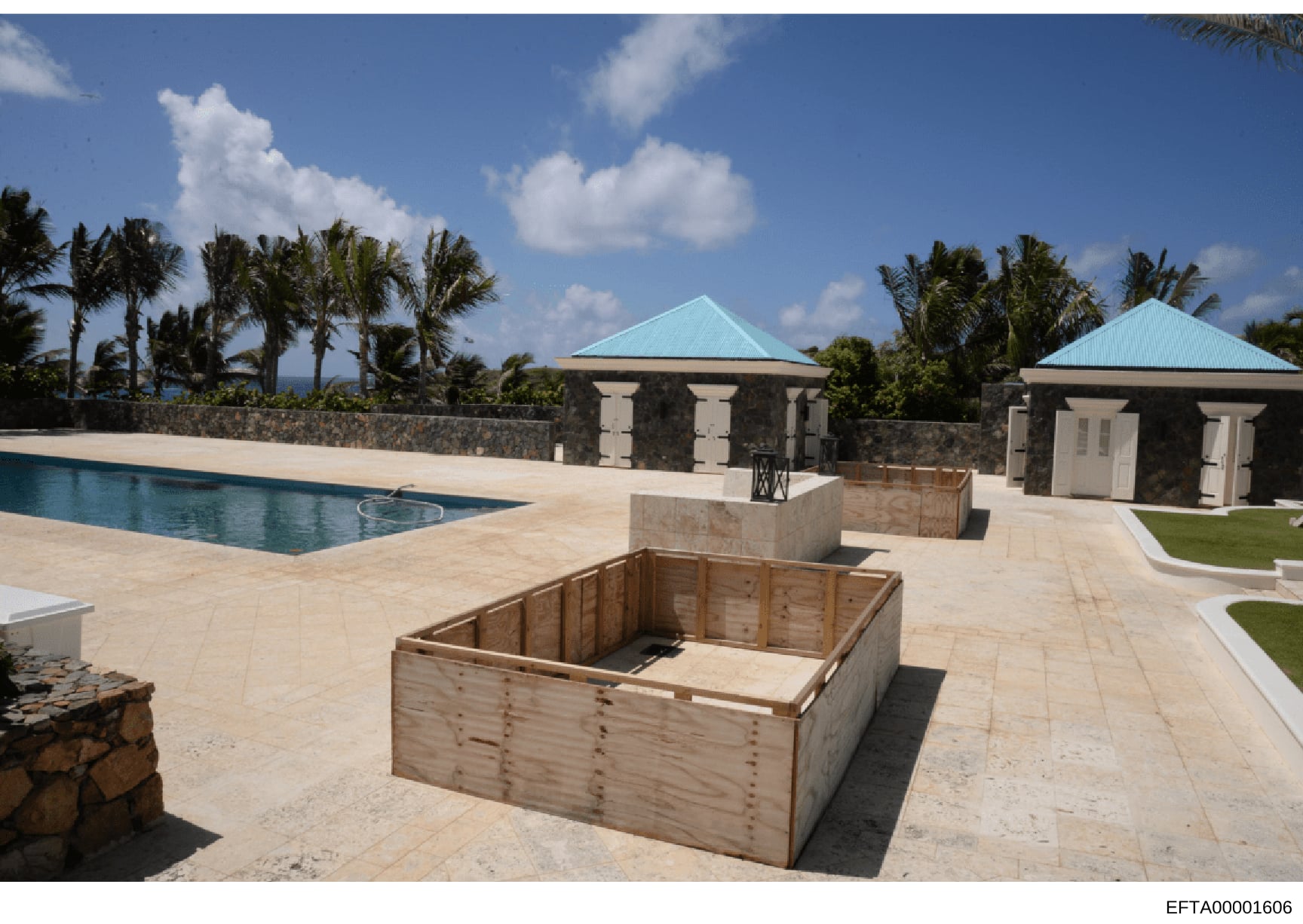 This photograph depicts an exterior view of a luxury estate property featuring a swimming pool, two stone cabanas with turquoise-colored roofs, manicured grounds, and extensive tropical palm tree landscaping. The image appears to be documentation of 