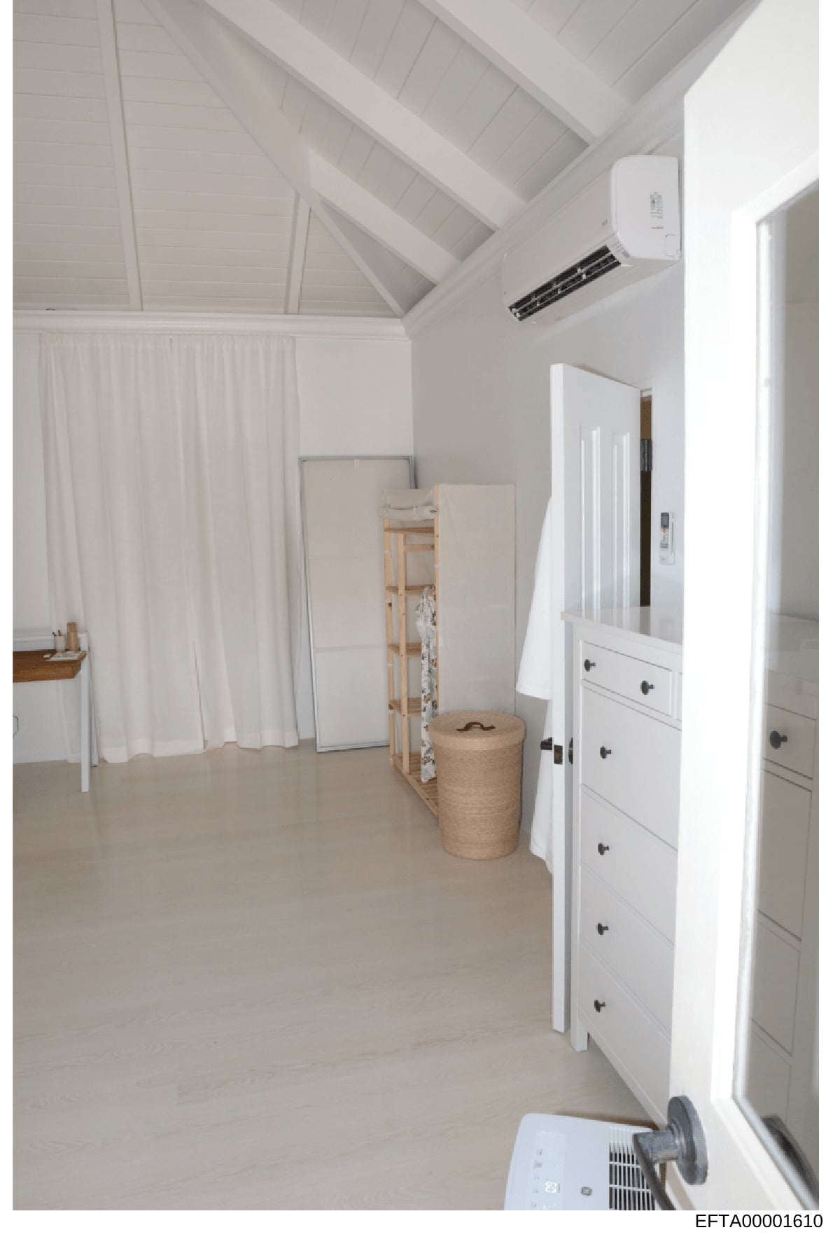 This is an evidence photograph showing the interior of a room with white walls, vaulted ceiling, and minimal furnishings. The space appears to be part of a residential property and contains white cabinetry, curtains, and storage items. This type of p