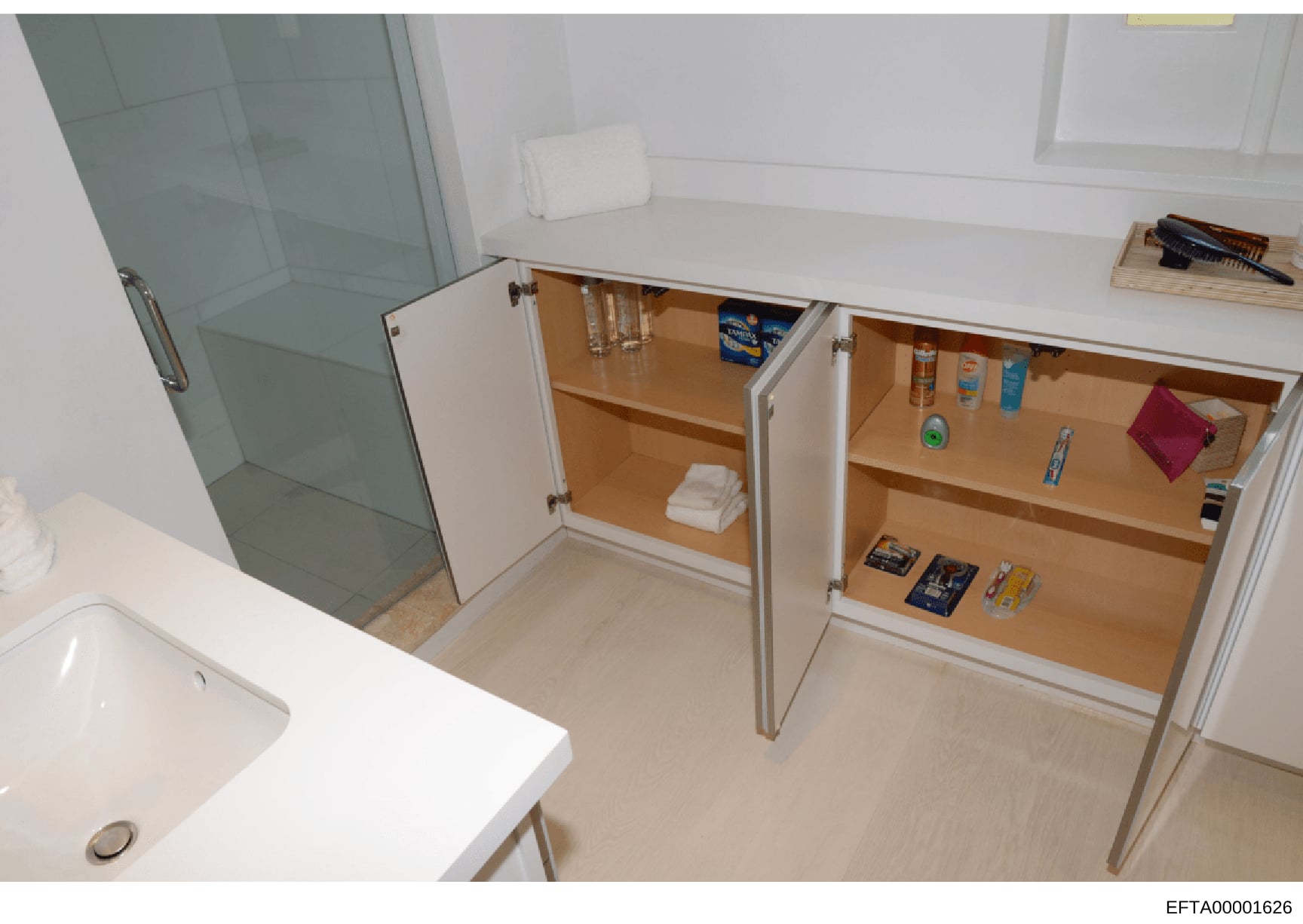 This photograph shows the interior of a bathroom with open medicine cabinet doors revealing stored items including toiletries, personal care products, and household supplies. The image documents the contents and layout of bathroom storage at what app