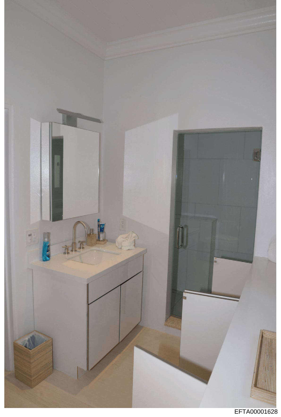 This is a photograph of a modern bathroom interior showing a white vanity with sink, medicine cabinet mirror, and a glass-enclosed shower area. The image appears to be documentation of property interior conditions, likely taken during an evidence or