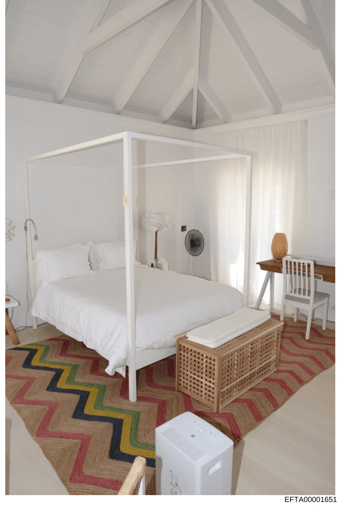 This is an interior photograph depicting a luxury bedroom with a white four-poster canopy bed, vaulted ceiling with exposed beams, modern furnishings, and decorative elements. The image appears to be documentation of a residential property interior, 