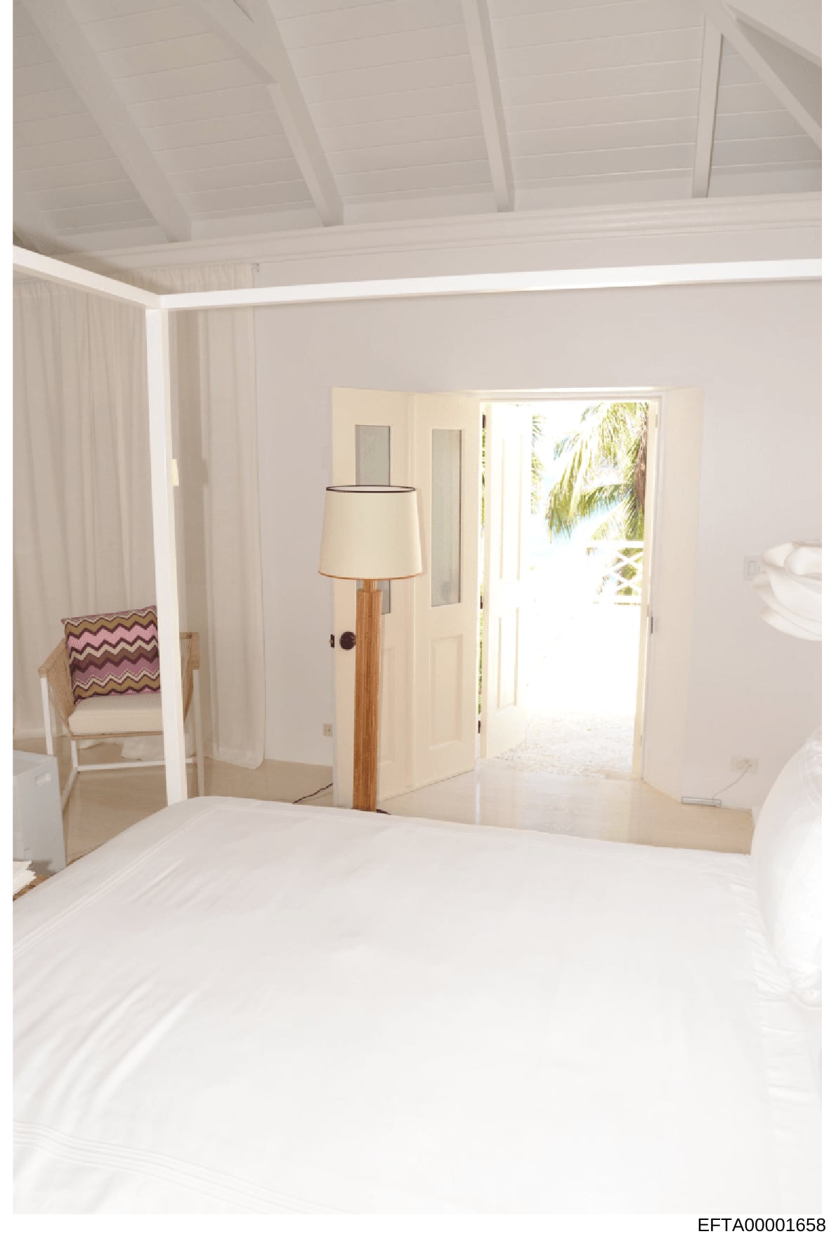 This is a photograph of a luxurious bedroom interior featuring all-white décor, likely from one of Jeffrey Epstein's properties. The image shows a spacious master suite with high ceilings, floor-to-door windows with views of tropical foliage, and con