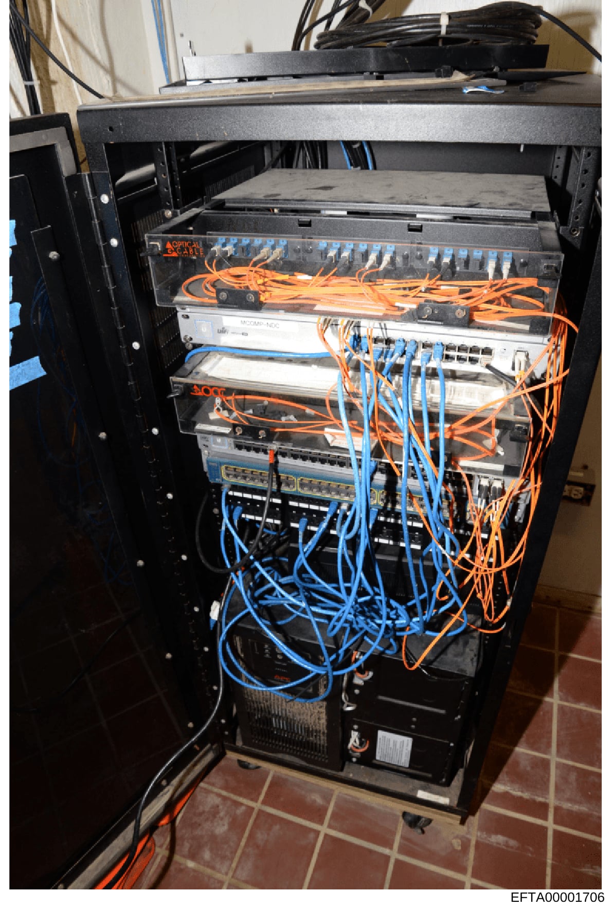 This photograph shows a professional network server rack containing optical scanning equipment, networking devices, and organized cabling in orange and blue. The equipment appears to be part of a data infrastructure system, likely seized as evidence 