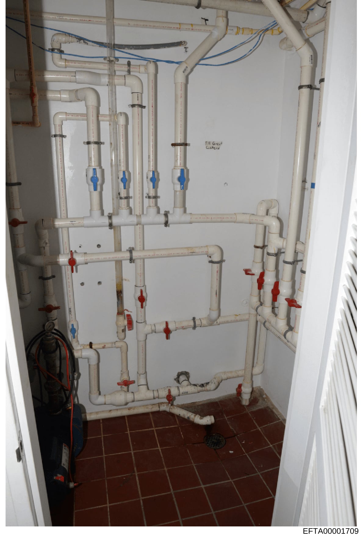 This photograph documents the internal plumbing infrastructure of a property, showing a comprehensive network of PVC pipes, valves, and electrical wiring in what appears to be a utility or mechanical room. The image captures the physical layout and c