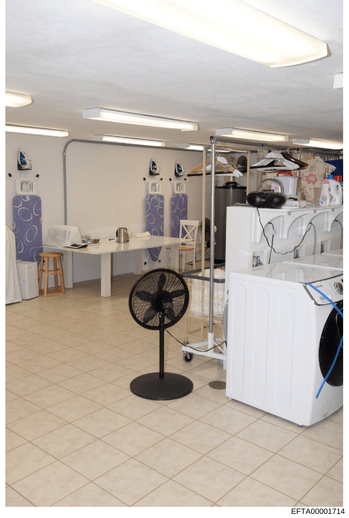 This photograph shows an interior room containing laundry facilities, basic living/work space, and storage. The room appears to be staff quarters or a utility area within a residential or commercial property, featuring washer/dryer units, ironing sta