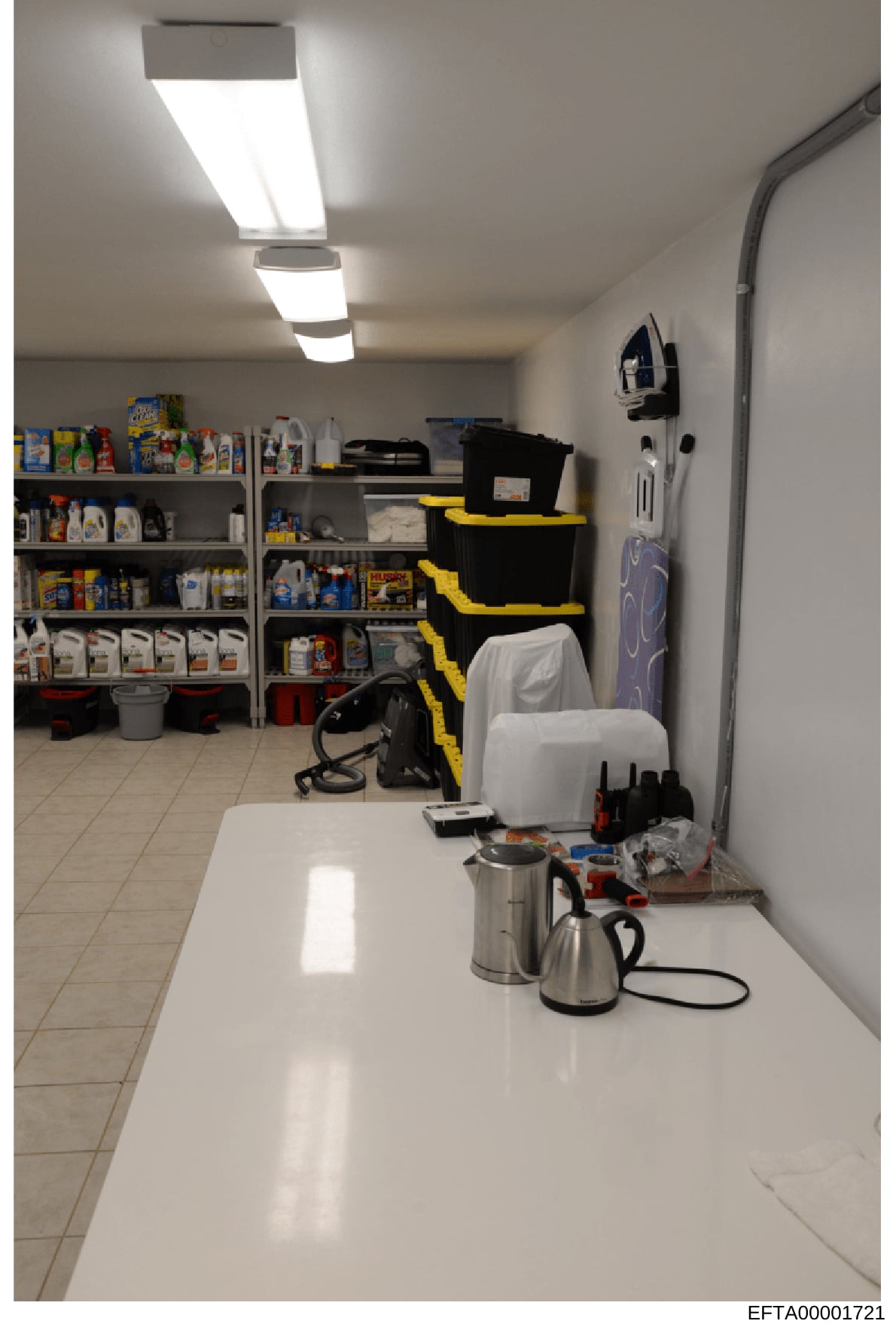 This is a photograph of a utility or storage room showing shelving units stocked with various household cleaning products, supplies, and equipment. The image documents the interior space of what appears to be a residential property, showing organized