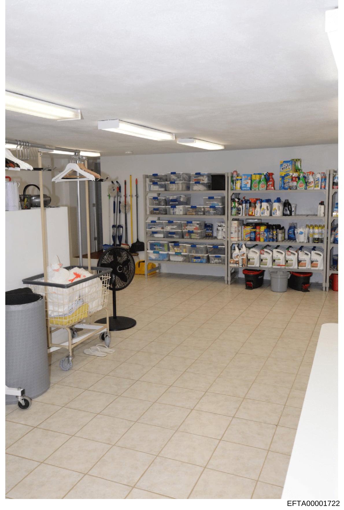 This is an interior photograph of a large, well-organized storage or utility room, likely part of a residential or commercial property. The space features extensive shelving containing numerous storage containers, cleaning supplies, household product