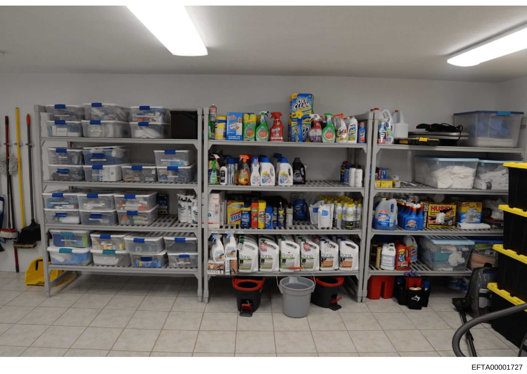 This photograph shows a well-organized storage area containing multiple shelves stocked with cleaning supplies, household products, and maintenance materials. The image captures what appears to be a utility or housekeeping storage room, likely from o