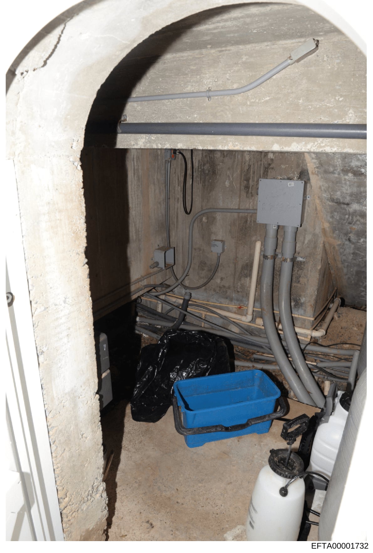 This is an evidence photograph showing an underground or basement mechanical room with electrical and plumbing infrastructure. The space contains electrical conduit, wiring, a blue plastic basin or drip tray, PVC piping, what appears to be a water he
