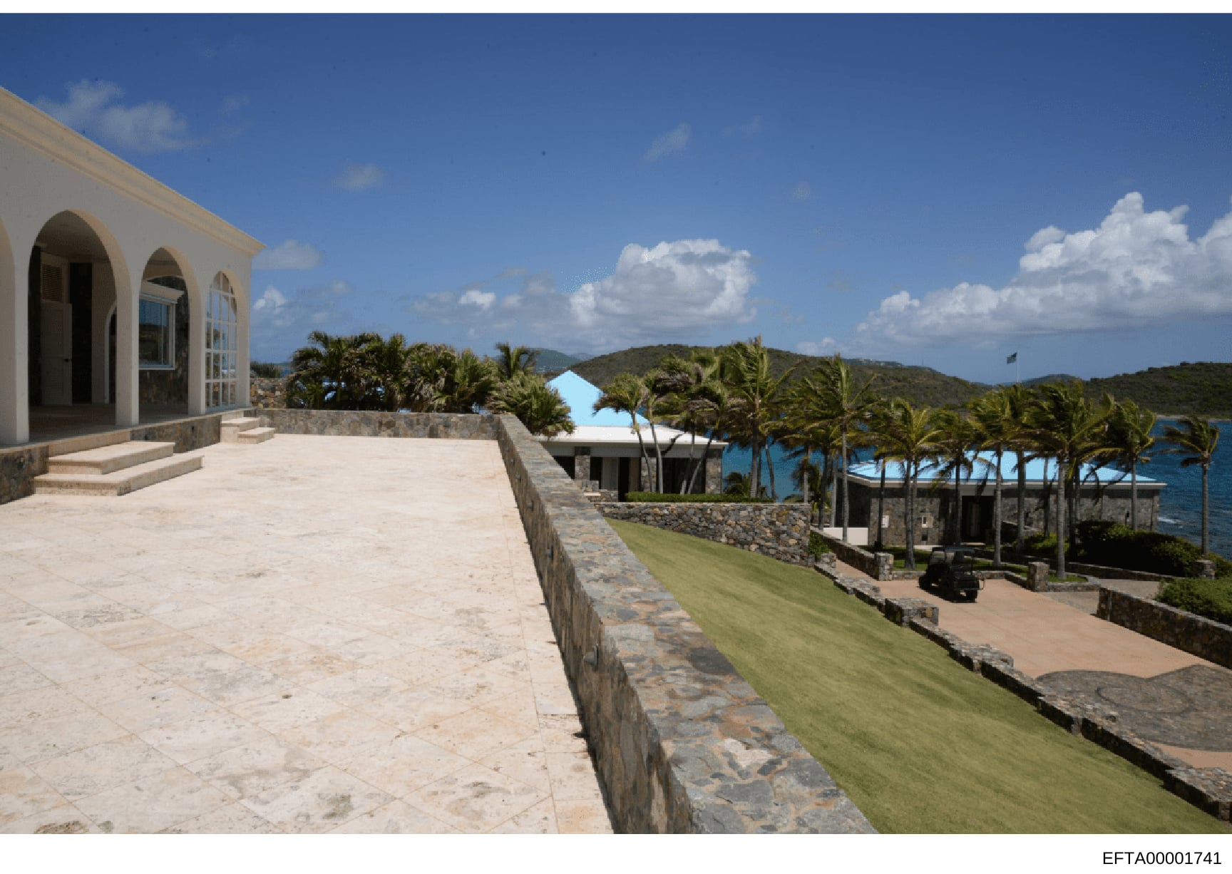 Photograph of a modern white residential building situated on a coastal property overlooking water and tropical islands. The structure features contemporary architecture with arched openings and is positioned on elevated terraces with manicured groun