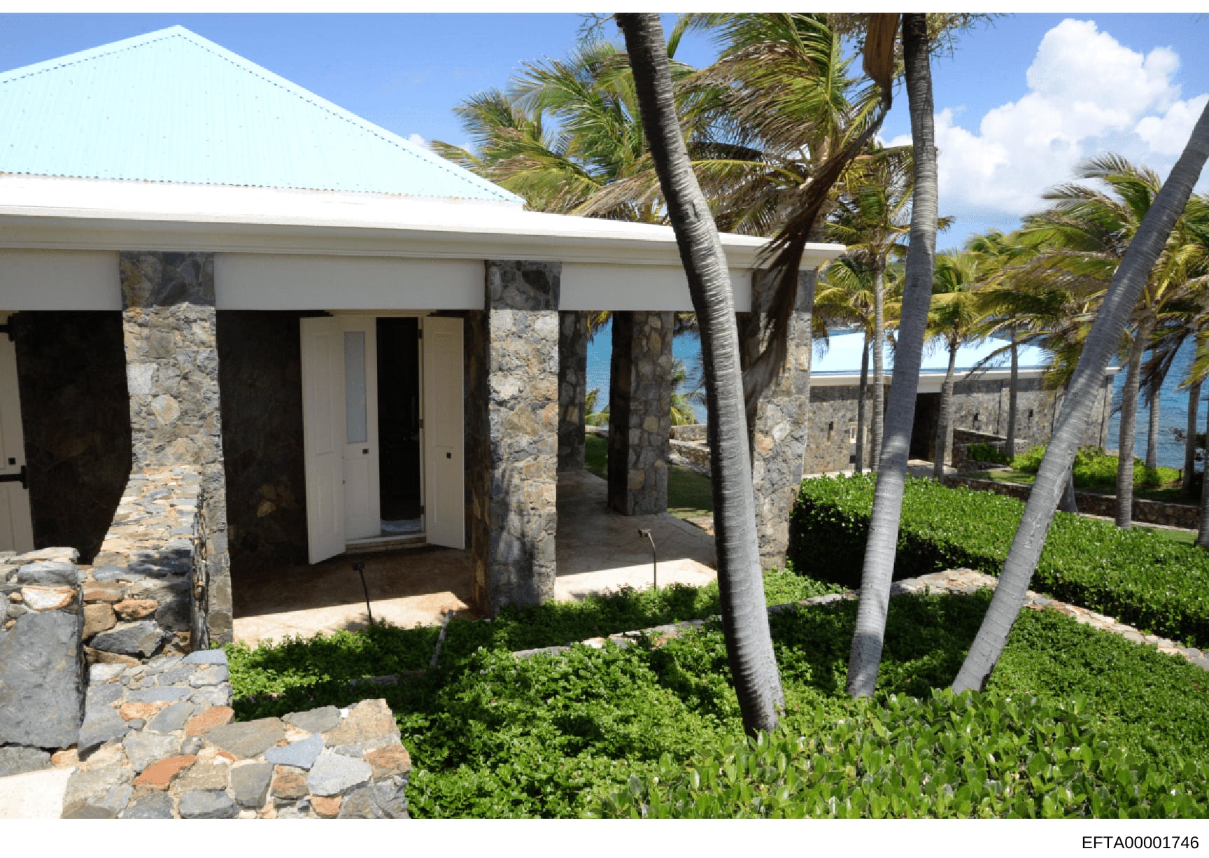 This is a photograph of a contemporary waterfront residence featuring stone and white architectural elements, palm trees, manicured landscaping, and ocean views. The image documents the exterior appearance of what appears to be a high-end coastal pro