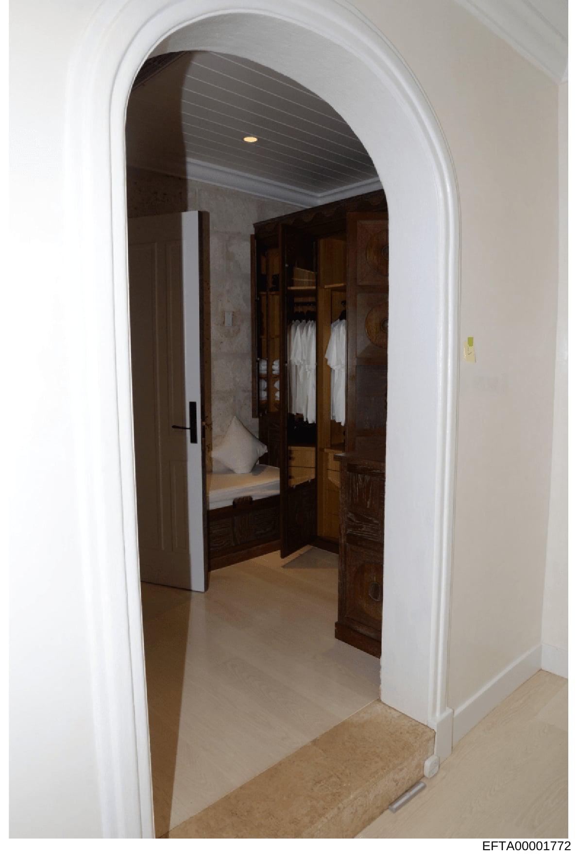 This is an evidence photograph showing the interior of a residential bedroom space, featuring an arched doorway entrance, a walk-in closet with dark wood cabinetry and mirrored doors, white towels visible on shelves, and what appears to be a connecte