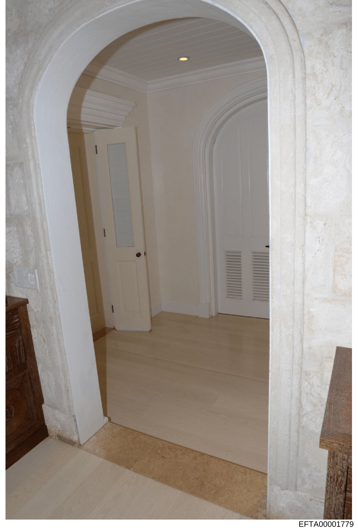 This is a photograph of an interior hallway featuring a distinctive curved archway entrance with cream-colored walls, white doors, recessed lighting, and light wood flooring. The image appears to be from a property inspection or documentation, likely