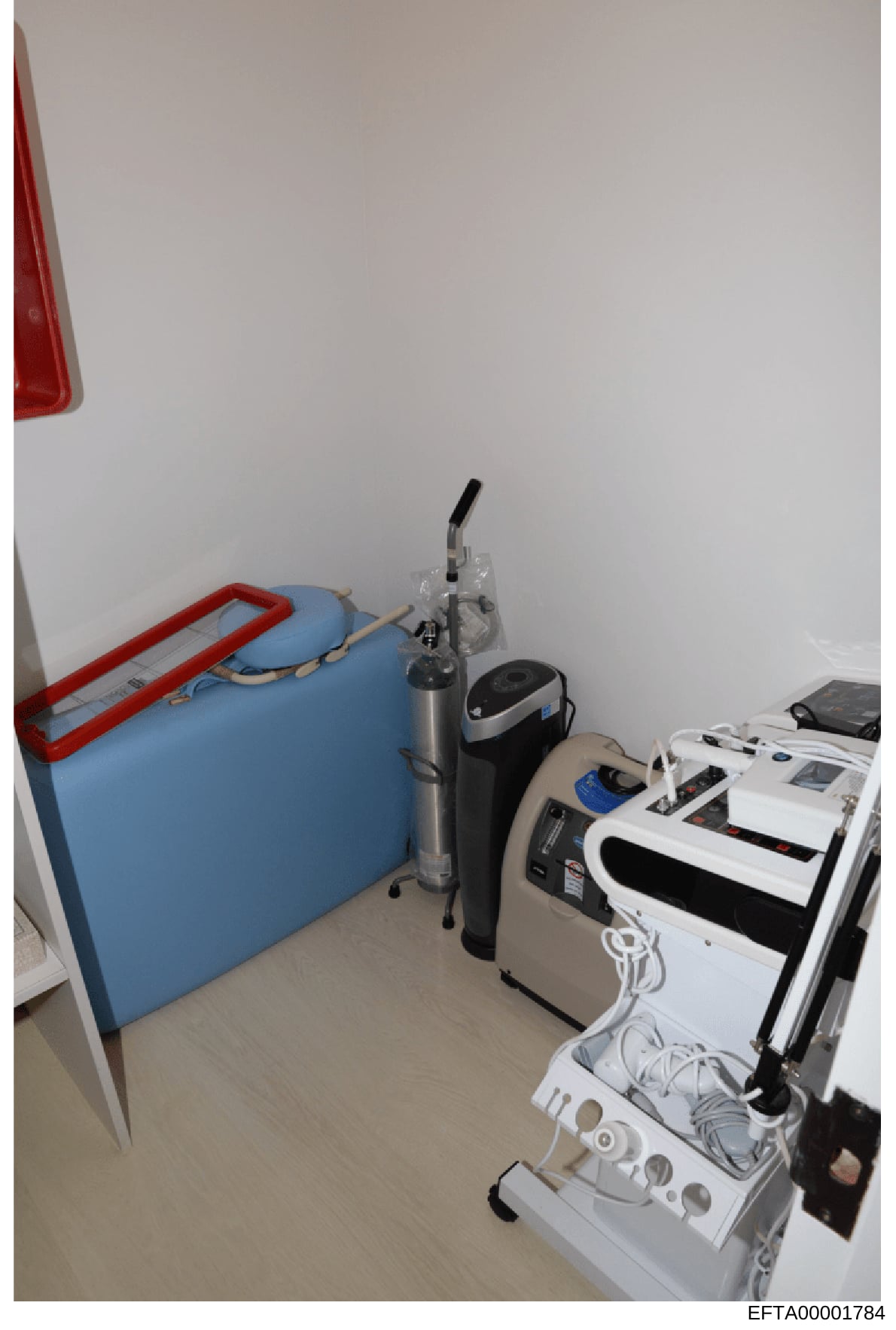 This is a photograph of an interior room containing various medical or therapeutic equipment. The image shows a blue padded mat or bed, professional medical devices, and white electronic equipment with power cords. The space appears to be a clinical