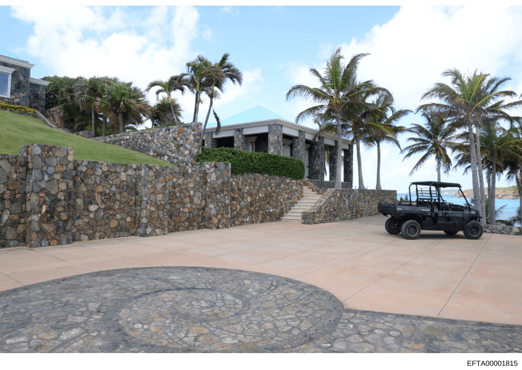 This photograph shows the exterior of a large residential property featuring modern stone construction, multiple levels built into a hillside, extensive stonework walls, and tropical palm trees. The property appears to be located on a coastal area wi