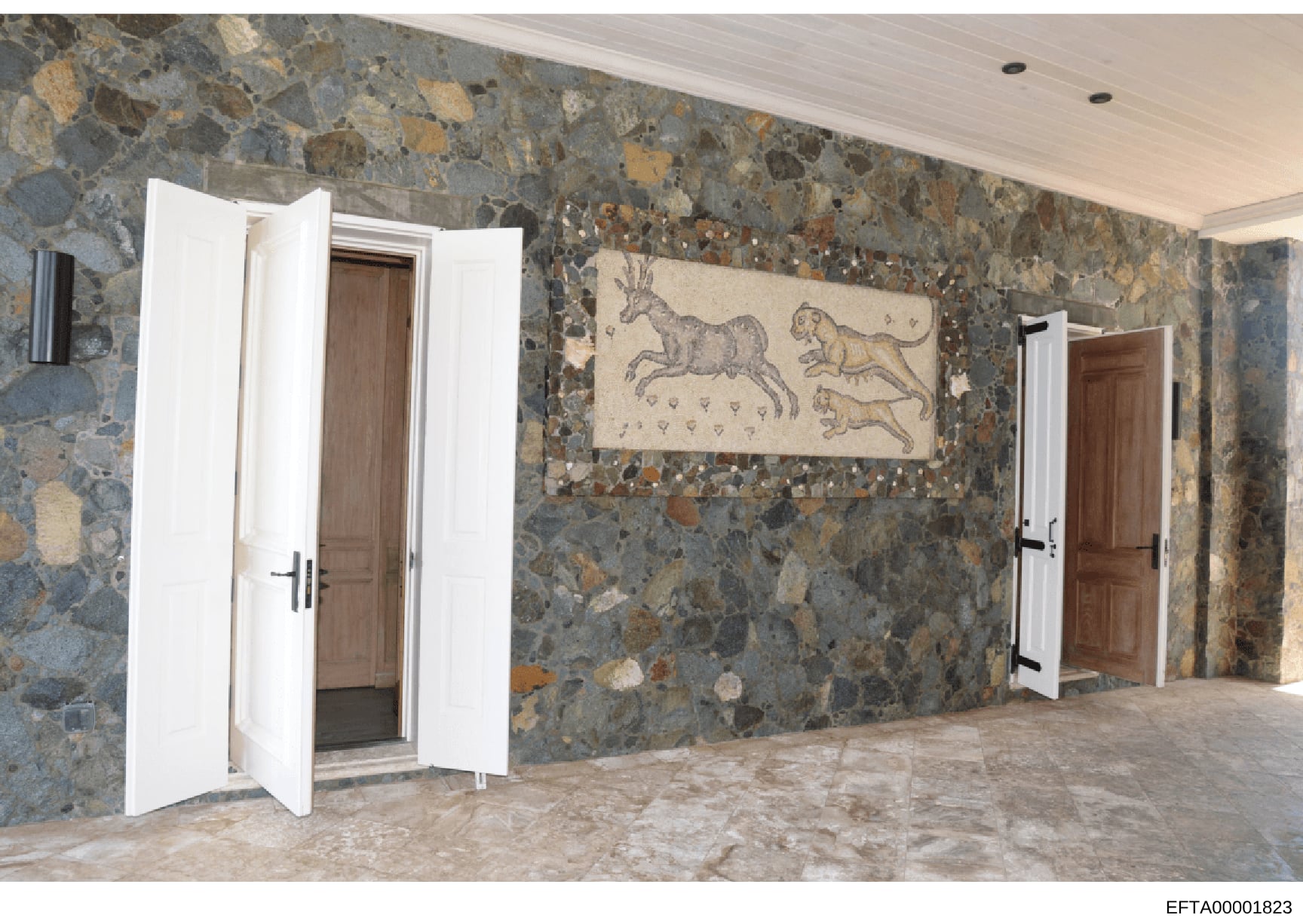 This photograph shows an interior room featuring distinctive multi-colored stone or aggregate wall treatment in earth tones (grays, golds, browns). The room contains white-trimmed wooden doors and a classical fresco or artwork depicting three horses