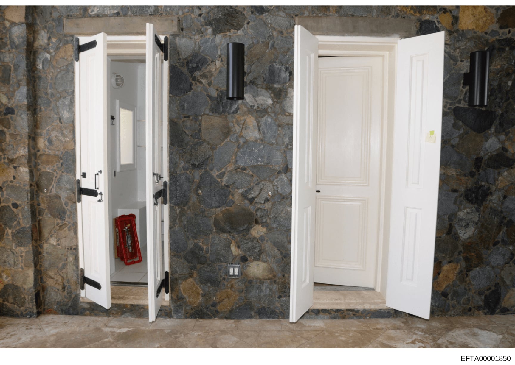 This photograph shows an interior hallway or corridor with two white painted double doors with black hardware, set against a distinctive mottled gray and brown stone or marble wall. A red fire extinguisher is visible inside the left doorway. The imag