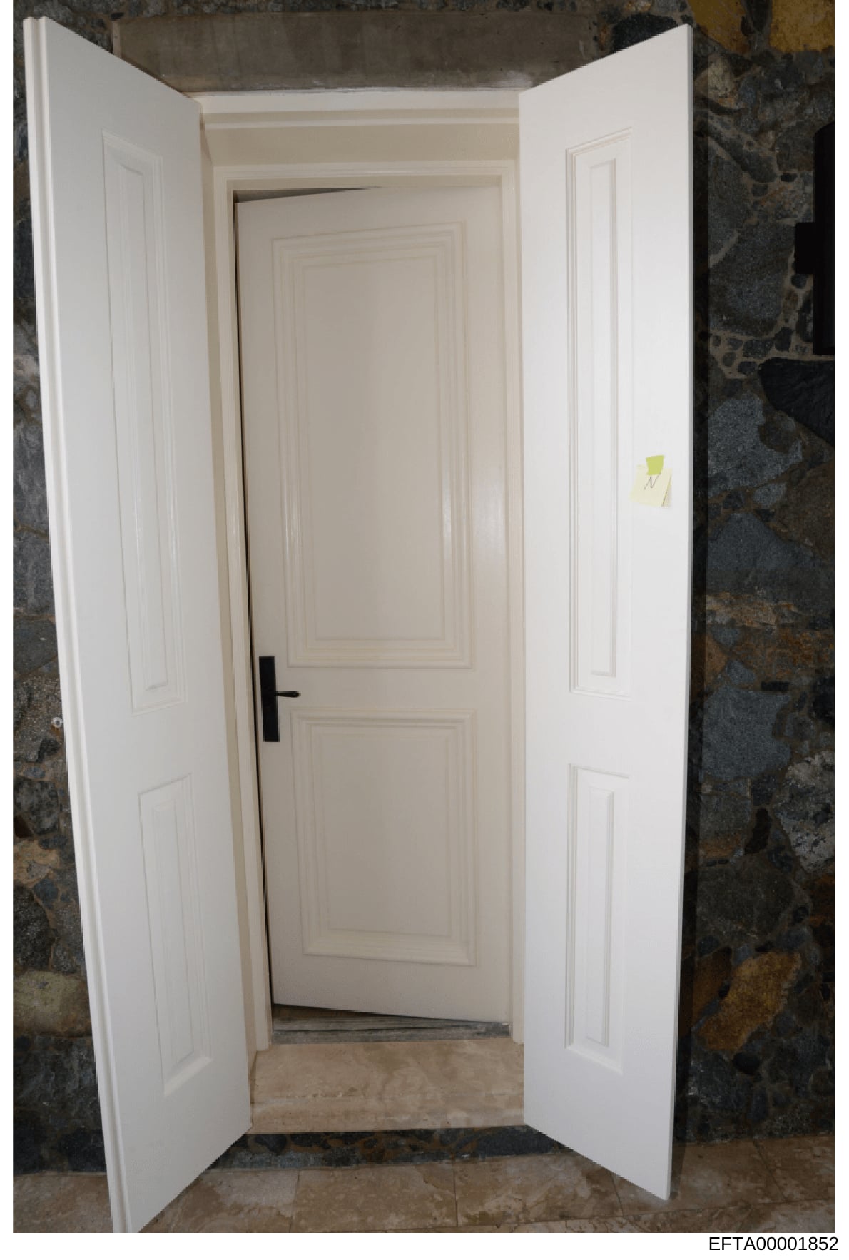 This is an evidence photograph depicting an interior doorway with white painted doors and frame. The image shows a two-door entrance opening into a room with stone or textured dark walls visible on either side. A yellow evidence marker or tag is visi