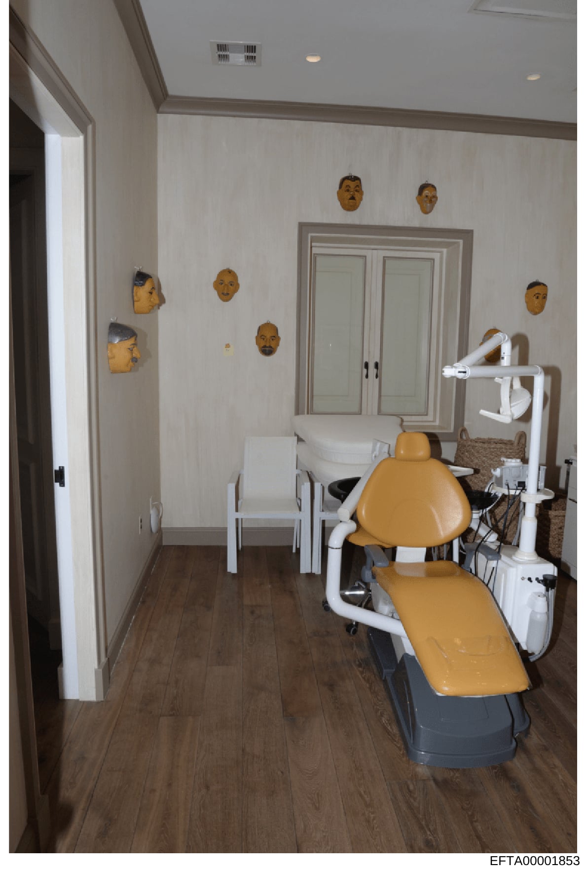 This photograph shows the interior of what appears to be a dental treatment facility or medical office space. The room features a dental chair with yellow upholstery, white equipment, and decorative wooden masks mounted on the walls. The image was ca