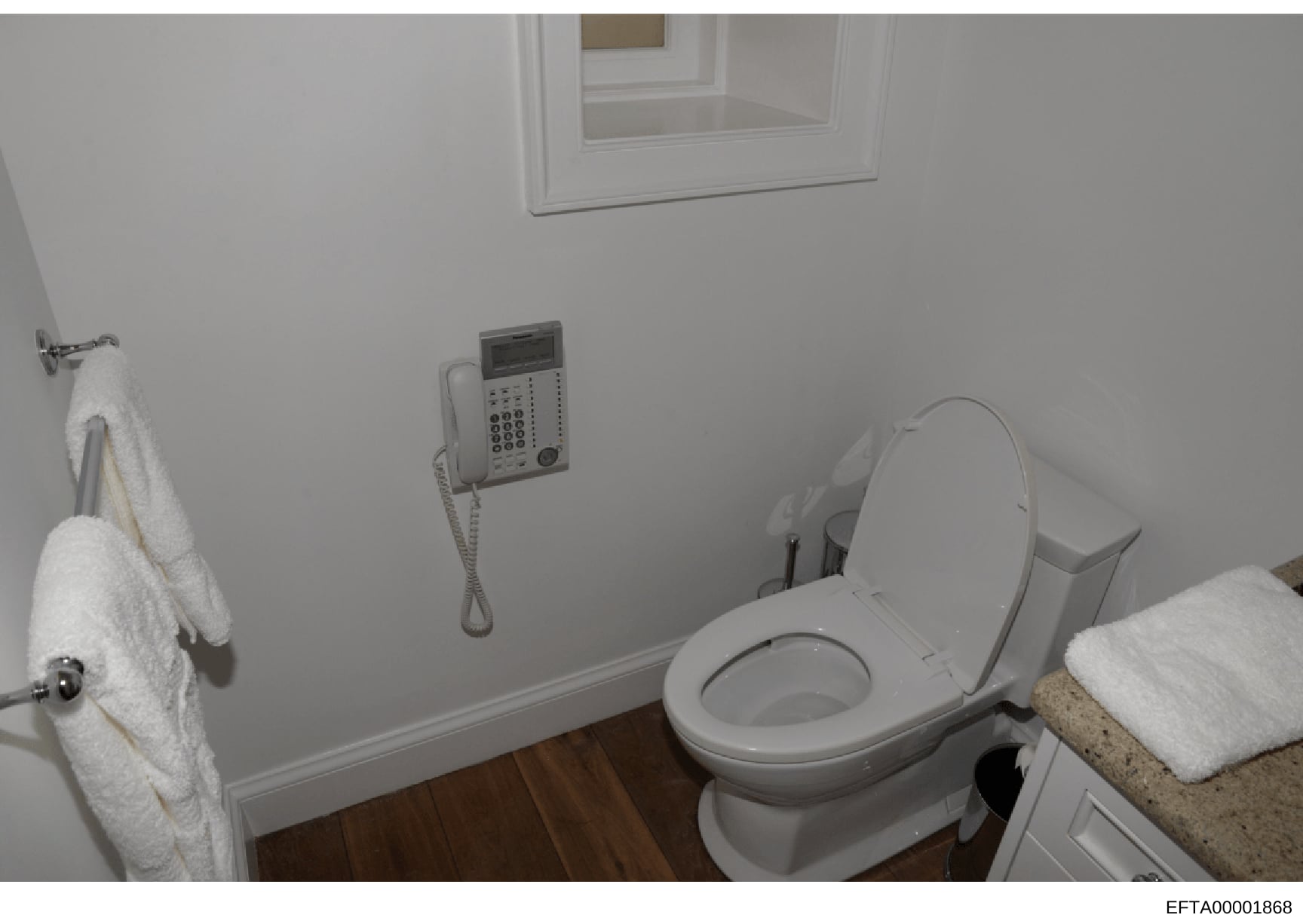 This is an evidence photograph of a bathroom interior showing a toilet with seat, sink with countertop, wall-mounted telephone, towel rack, and cabinet storage. The image appears to be from a property inspection or evidence documentation related to t