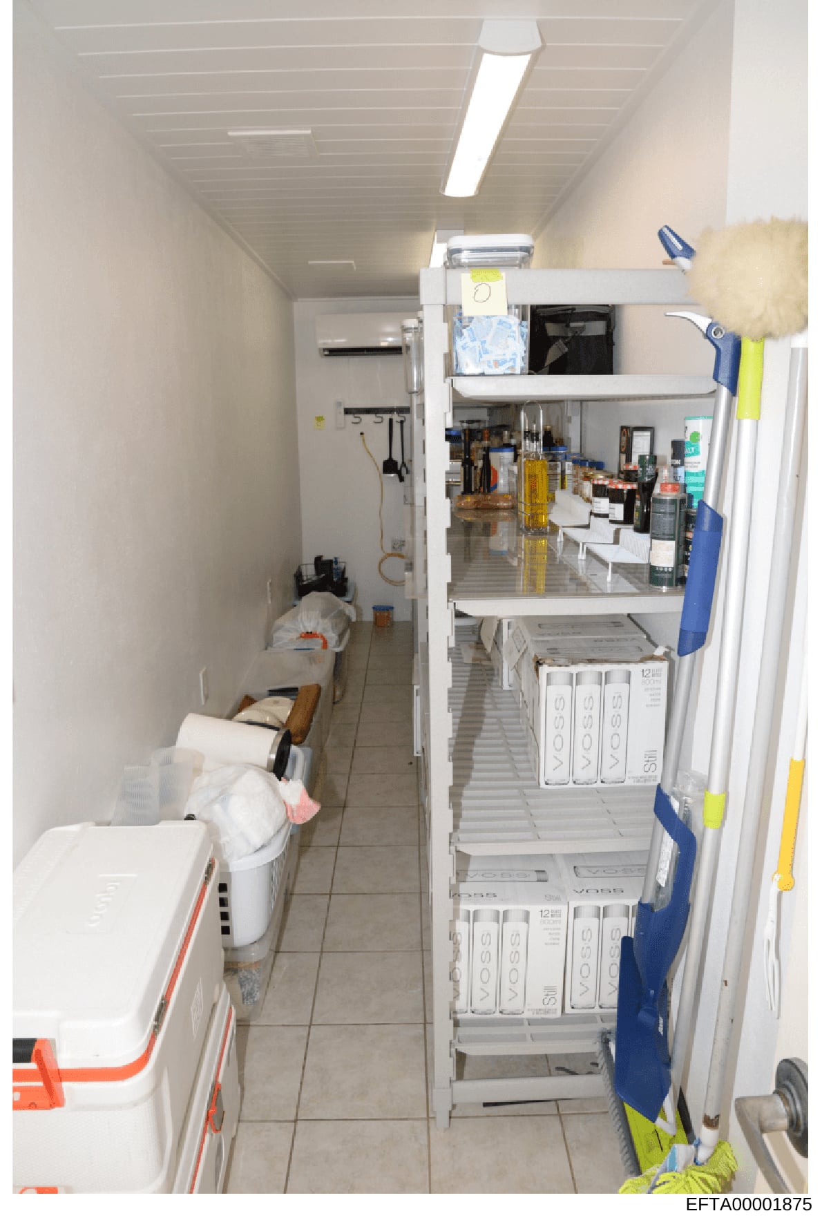 This is an evidence photograph showing the interior of a narrow utility or storage room, possibly a kitchen pantry or supply closet. The room contains white appliances including what appears to be a freezer or refrigerator on the left, shelving units