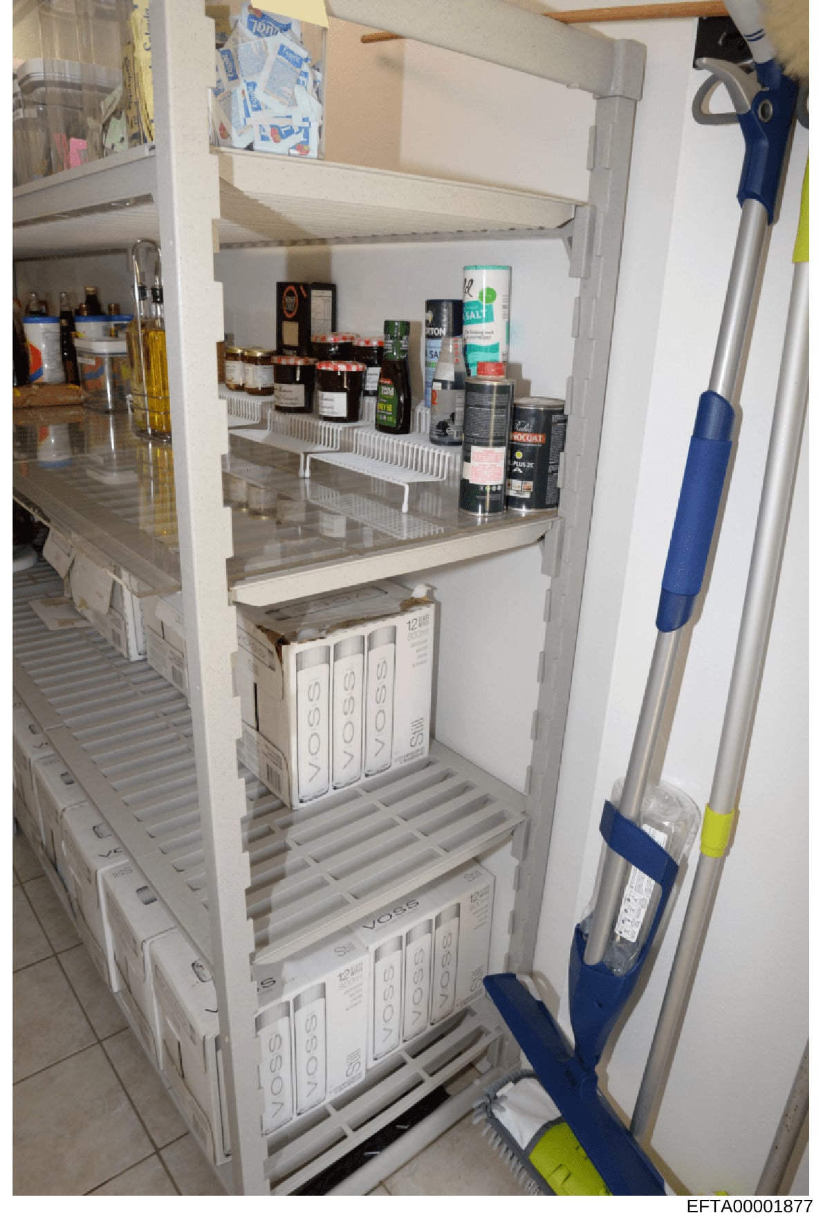This is an evidence photograph showing the interior of a kitchen pantry with open shelving and storage. The image captures various food items, household supplies, and cleaning products organized on multiple shelves, along with what appear to be water
