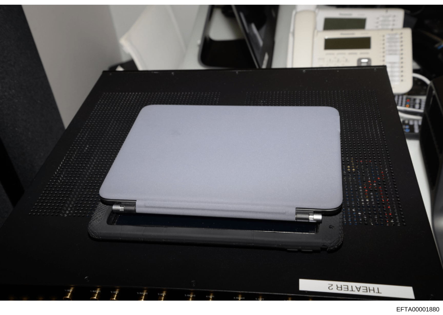This is a photograph of a silver laptop computer (appears to be an HP or similar model) placed on a black textured mat, likely taken during an evidence collection or forensic examination. The laptop is positioned in what appears to be an office or in