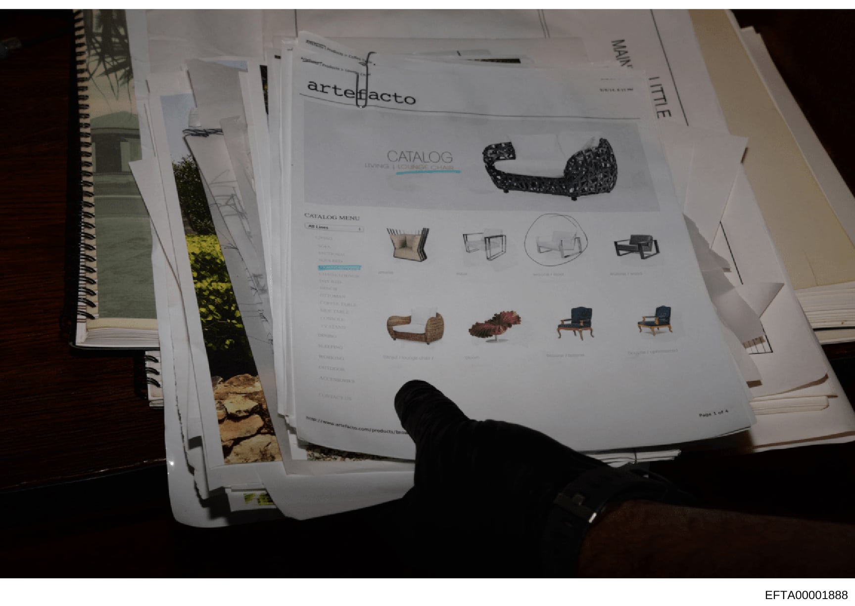 This photograph shows a collection of printed materials including an Artefacto furniture catalog and architectural/interior design documents. The catalog displays contemporary furniture pieces including upholstered seating, tables, and chairs. This a