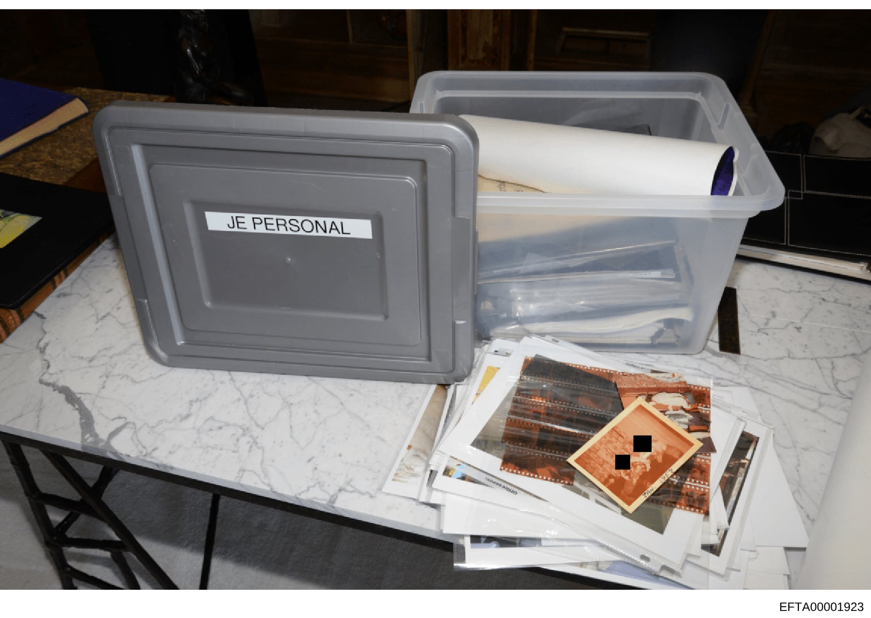 This photograph documents evidence seized during the investigation, showing two gray plastic storage containers labeled 'JE PERSONAL' containing documents and materials. One container is open and filled with papers and files; the other is closed with