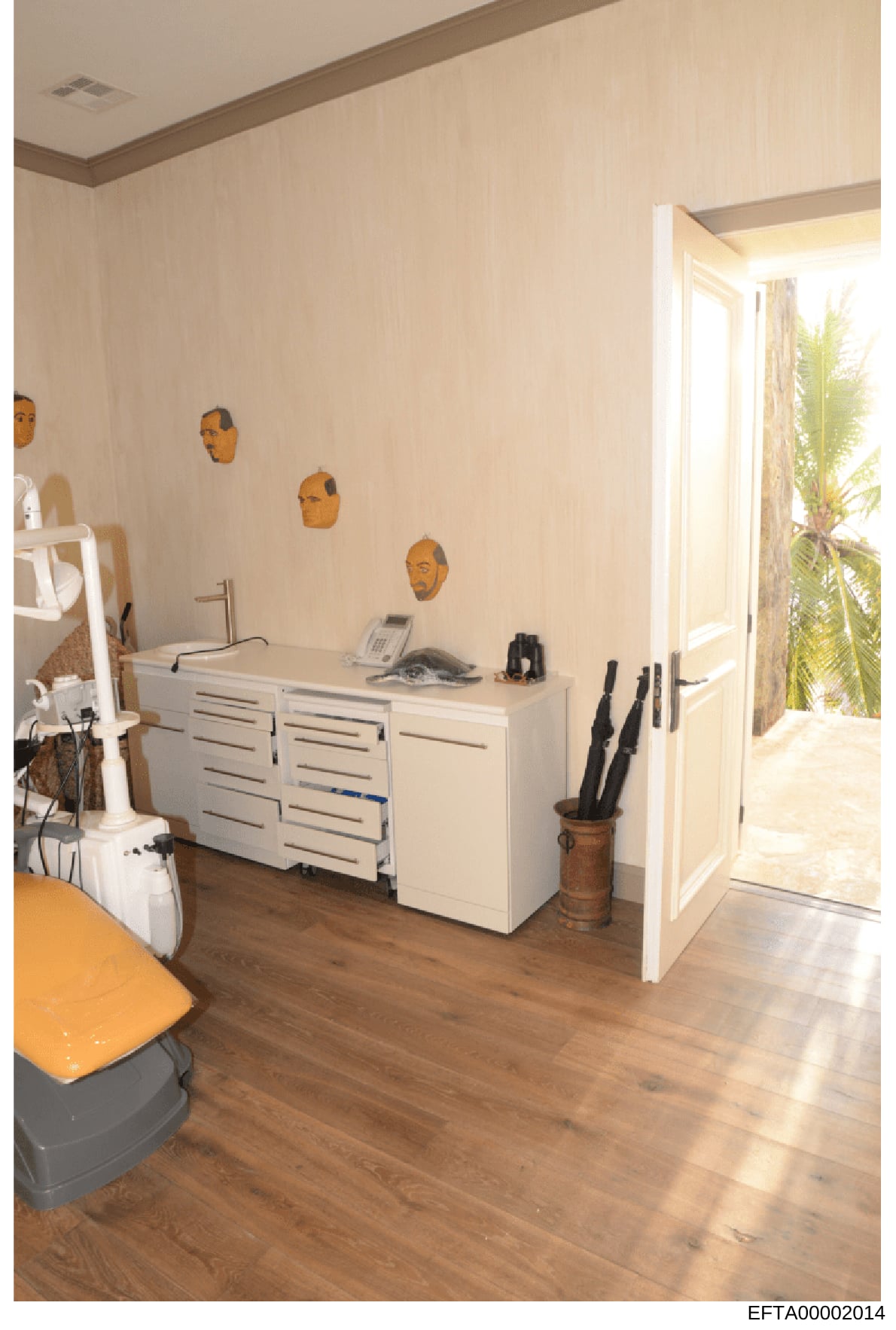 This is a photograph of an interior space featuring a modern bathroom or dressing room with cream-colored walls, wooden flooring, and contemporary furnishings. The room displays four golden sculptural head pieces mounted on the wall above a white sto