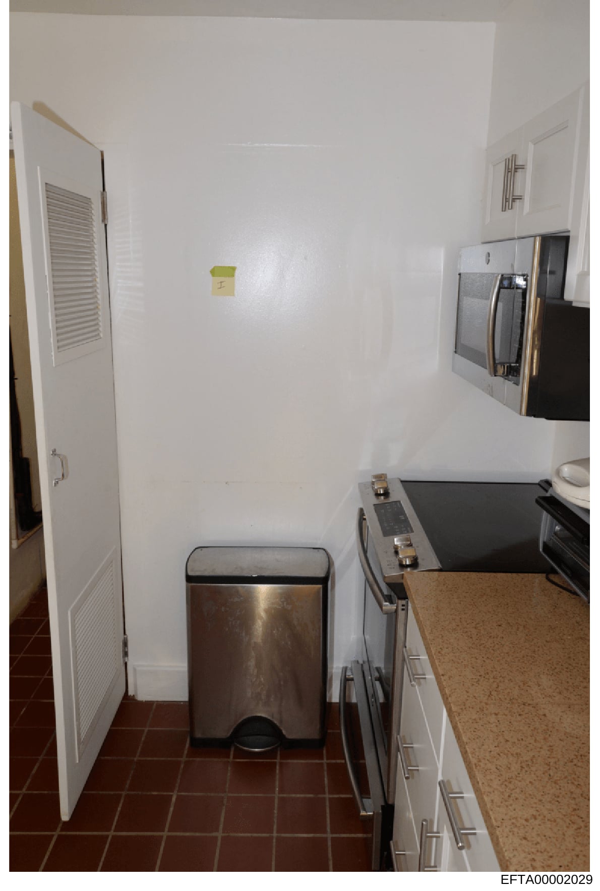 This is a photograph of a residential kitchen interior, showing appliances, countertops, and storage areas. The image appears to be evidence documentation from a property inspection related to the investigation, with a Bates stamp indicating it is pa