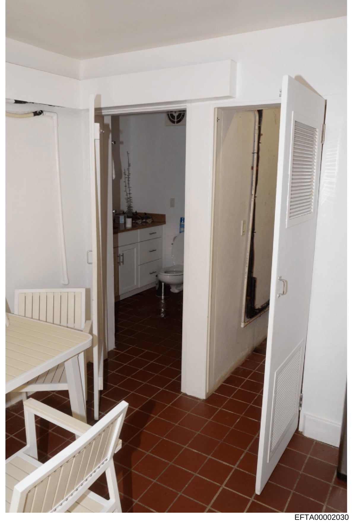 This photograph shows the interior of a kitchen and connected bathroom space, featuring white cabinetry, dark tile flooring, and various household appliances. The image appears to be evidence documentation from a property inspection or seizure relate