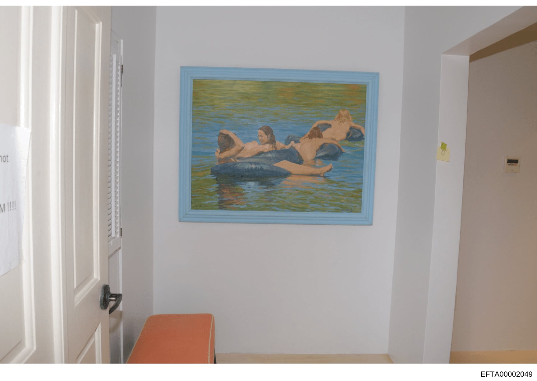 This is a photograph of an interior room showing a framed painting or artwork hung on a white wall. The artwork depicts multiple figures in water with inflatable tubes or floats. The photo appears to be evidence documentation from the investigation,