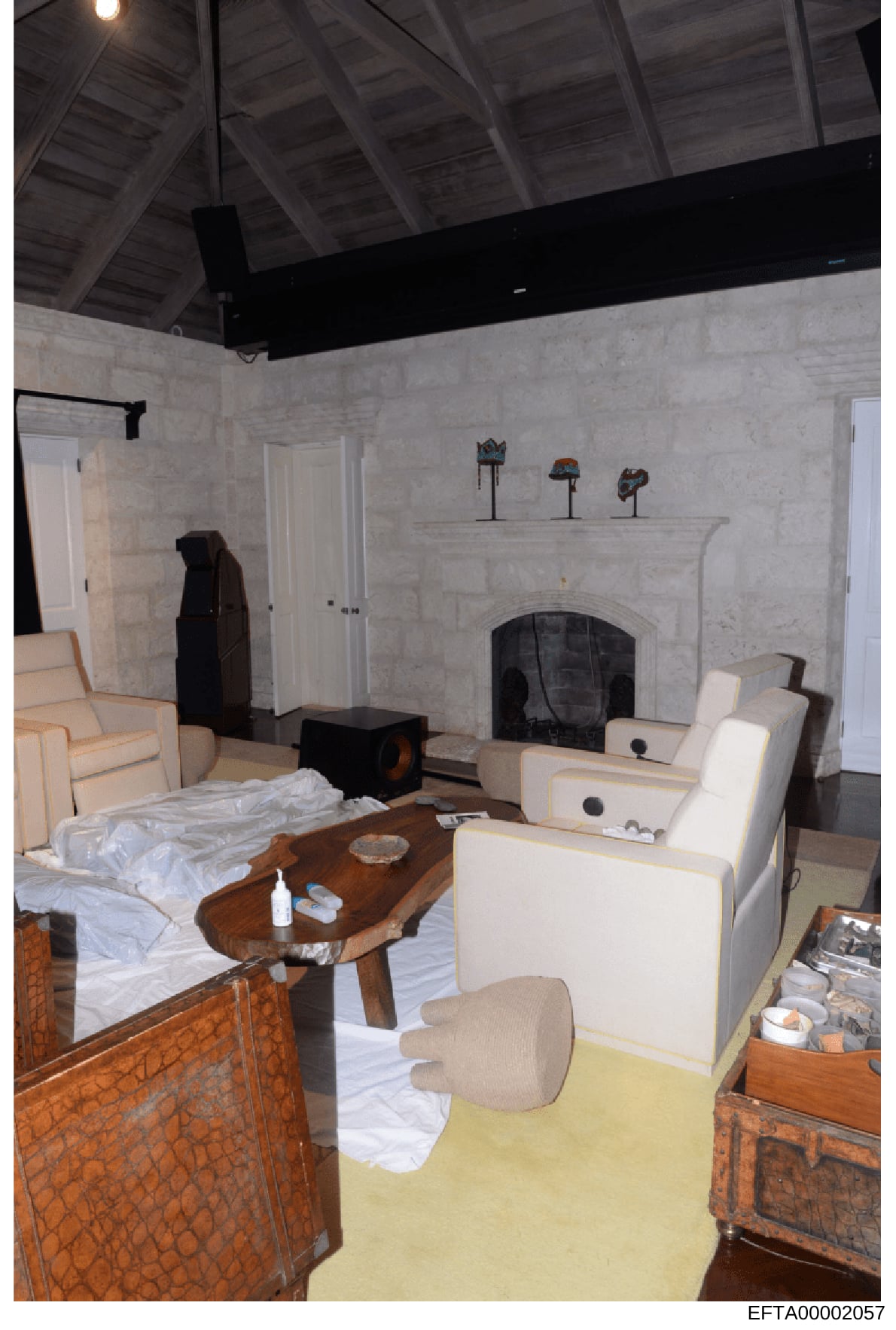 This is a photograph of an interior room featuring a marble fireplace, cream-colored upholstered furniture, wooden tables, and decorative items on a mantelpiece. The room appears to be part of a residential property under investigation, likely docume