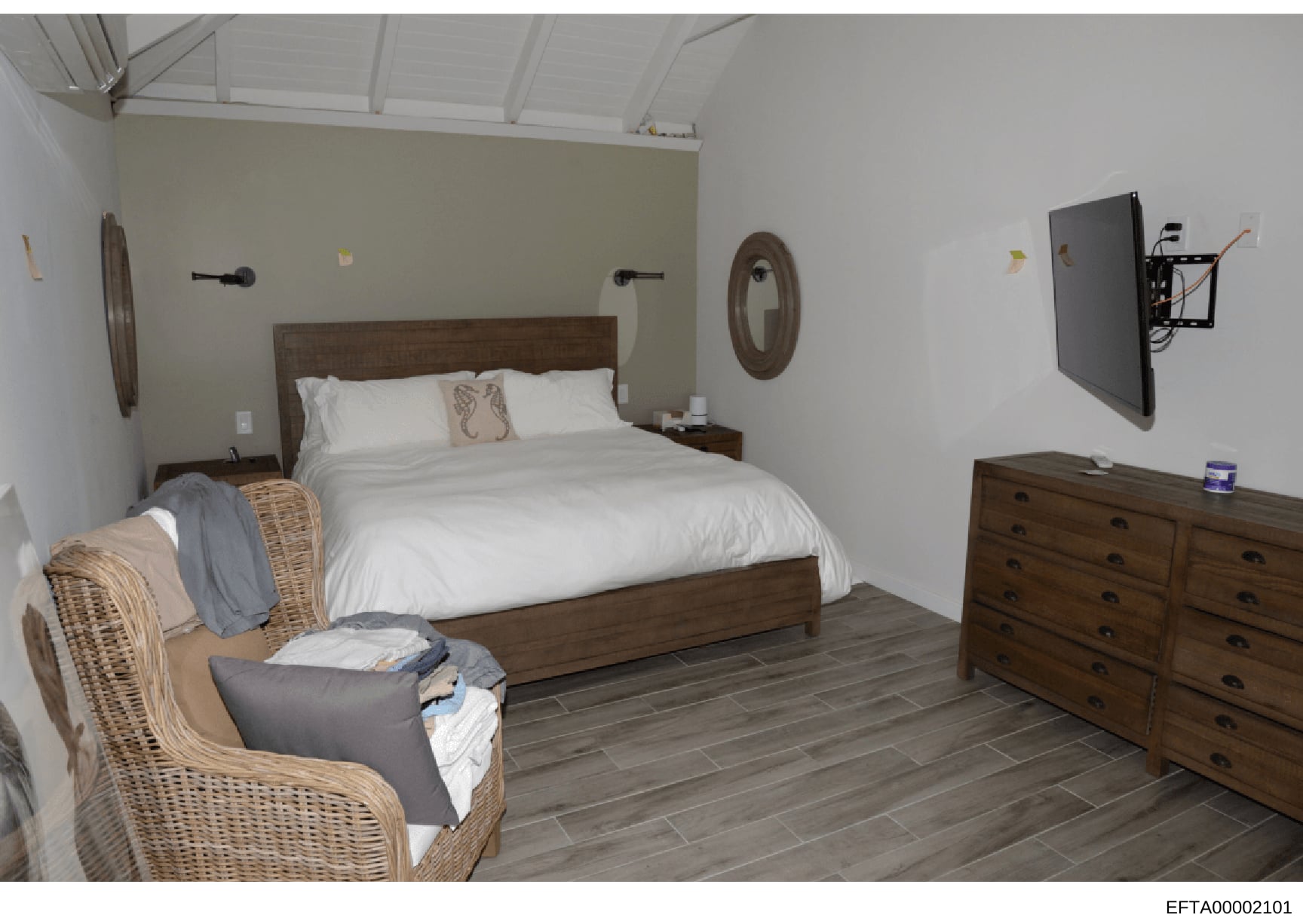 This is a photograph of a furnished bedroom interior, likely from one of Jeffrey Epstein's properties. The room features a wooden bed frame, matching wooden dresser, wicker chair, and coastal-themed decorative elements. The image appears to be eviden