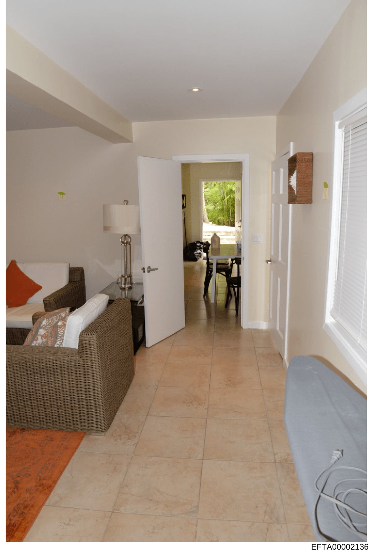 This is a photograph of a modern residential interior space showing a hallway or corridor connecting multiple rooms. The image depicts living quarters with contemporary furnishings, tile flooring, cream-colored walls, and natural lighting. The space
