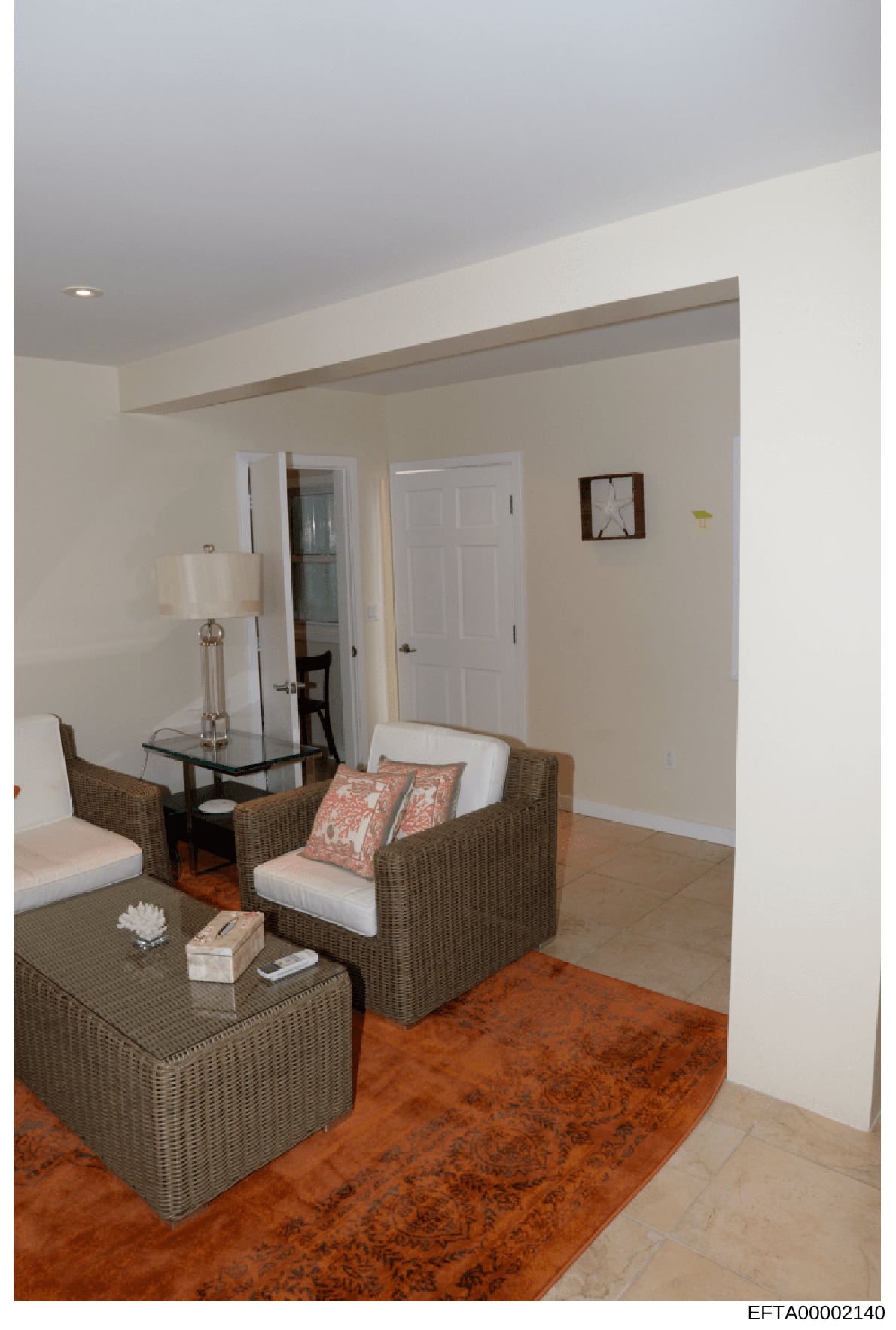 This is a photograph of a residential interior room featuring contemporary furnishings. The space shows a seating area with wicker furniture, neutral décor, and minimal personal items. The photo appears to be documentation of property interior condit