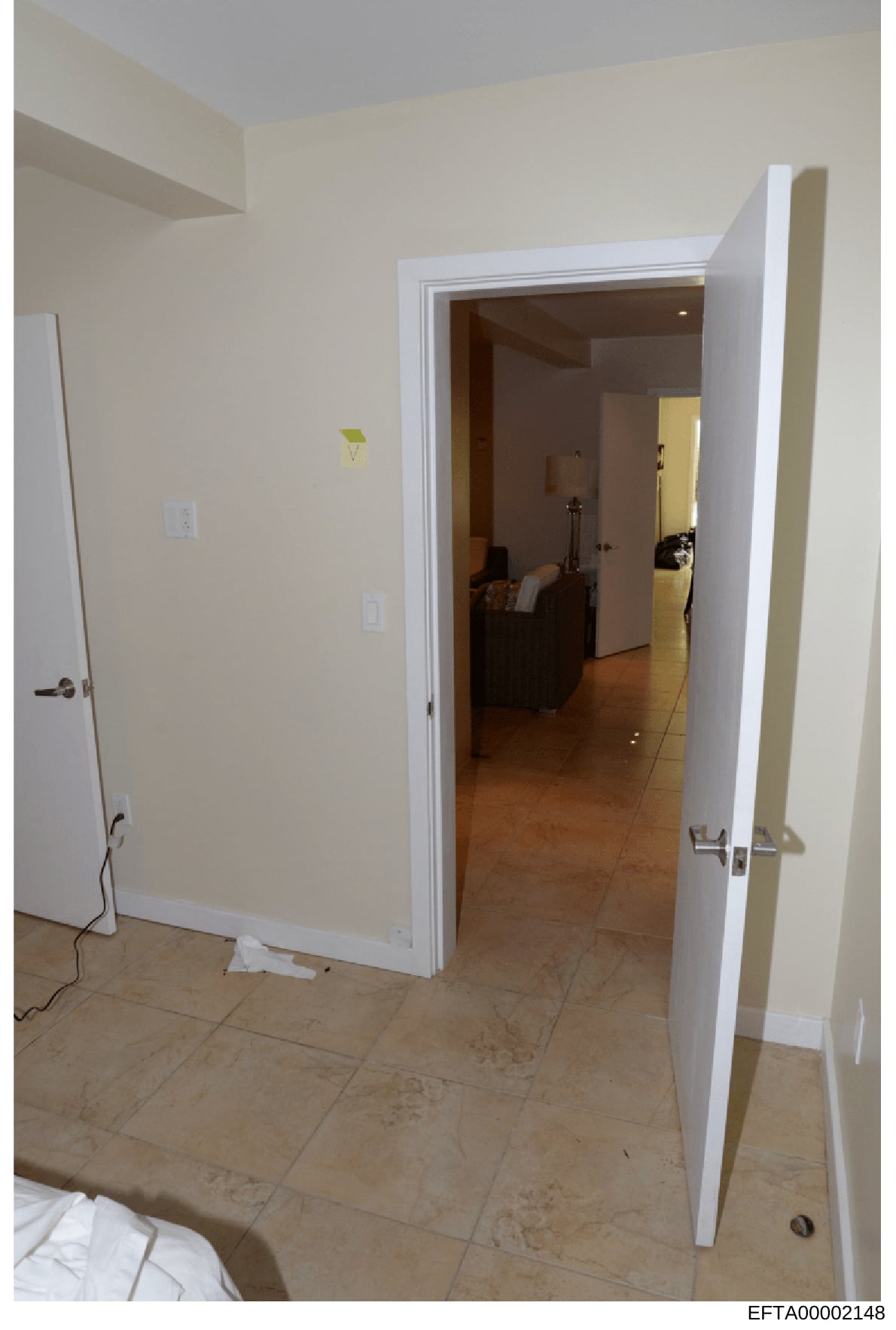 This is a photograph of an interior residential space showing a doorway with white trim leading into an adjacent room with dark wood flooring. The image captures beige/cream-colored walls, recessed shelving on the left, electrical outlets, and a view