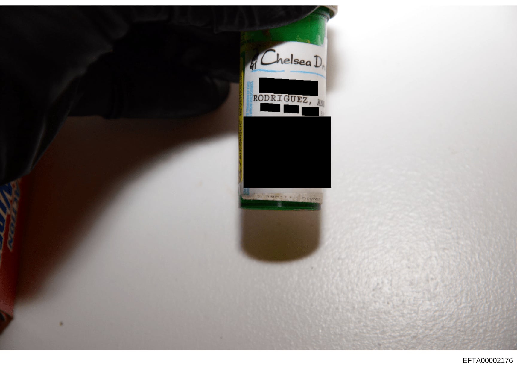 This is a photograph of a bottle with a handwritten label identifying it as belonging to 'Chelsea D.' with the name 'RODRIGUEZ, AM' partially visible beneath redacted sections. The bottle contains a clear or light-colored liquid and appears to be evi