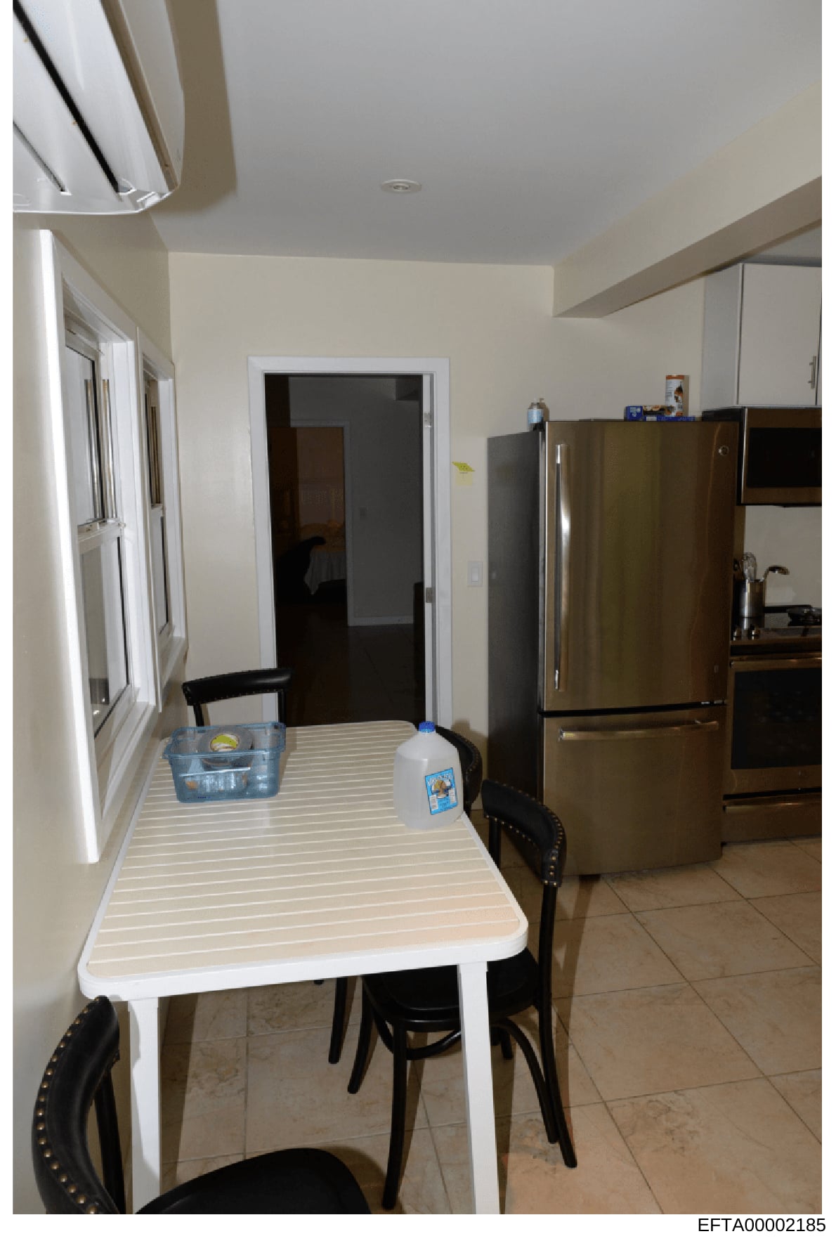 This photograph shows a residential kitchen interior, featuring a dining area with a white table and black chairs, stainless steel refrigerator, and various kitchen appliances and fixtures. The image appears to be documentation of a property space, l